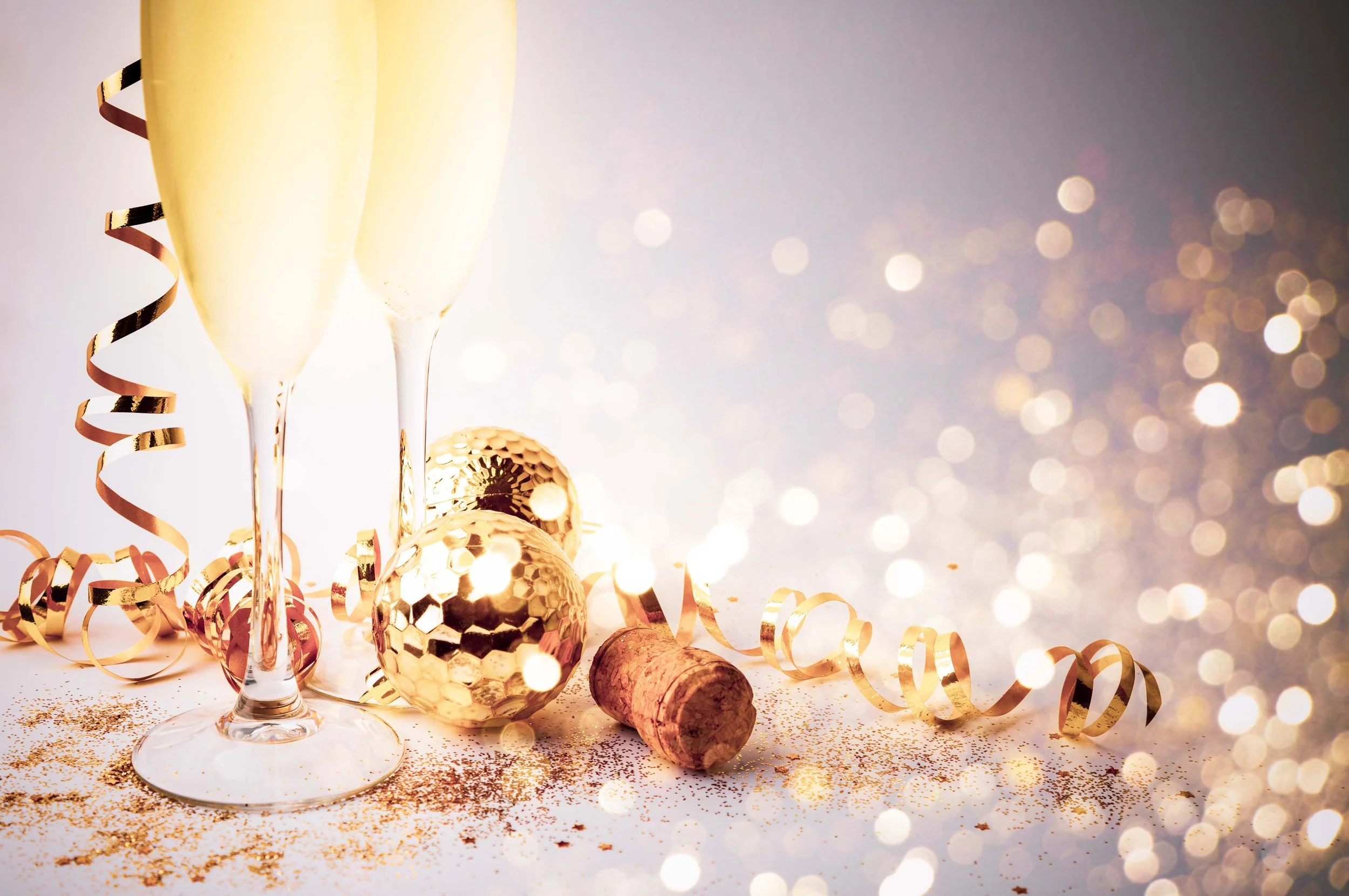 Two champagne glasses, gold glitter, and gold foil balloons with confetti and curly ribbons on a festive background