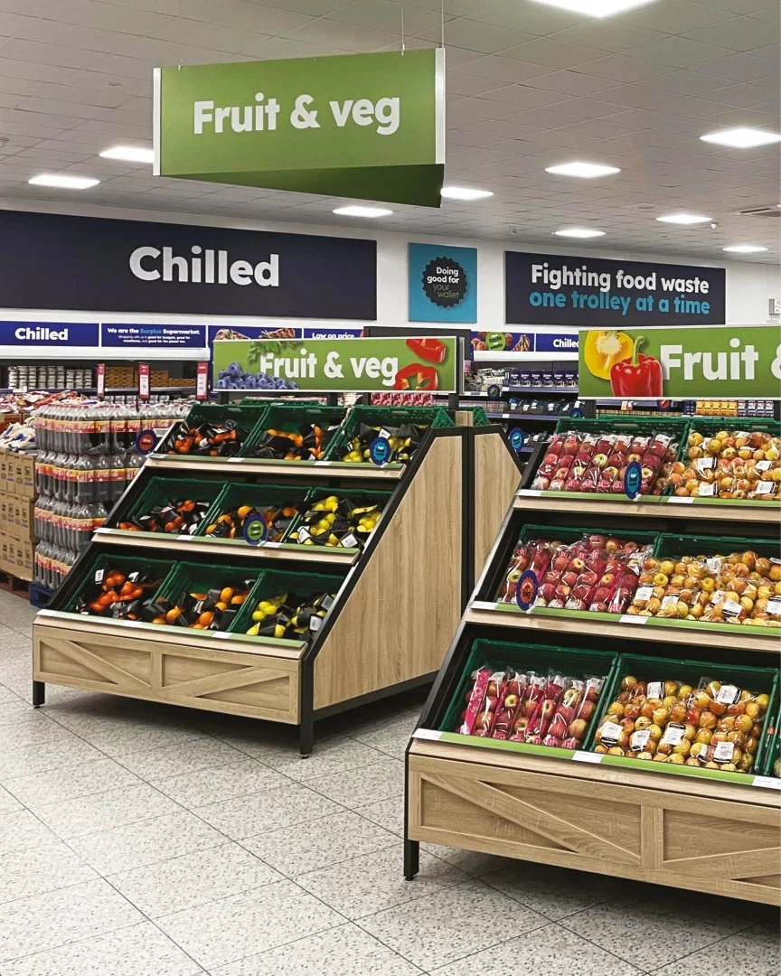 Interior of a cozy restaurant with wooden furniture, white pendant lights, and large windows letting in natural light. The tables are set with plates, glasses, and flowers.