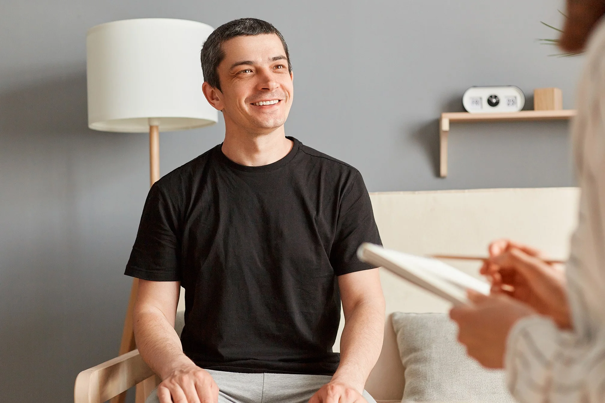 A man smiling during a therapy session with a therapist taking notes in a notepad.