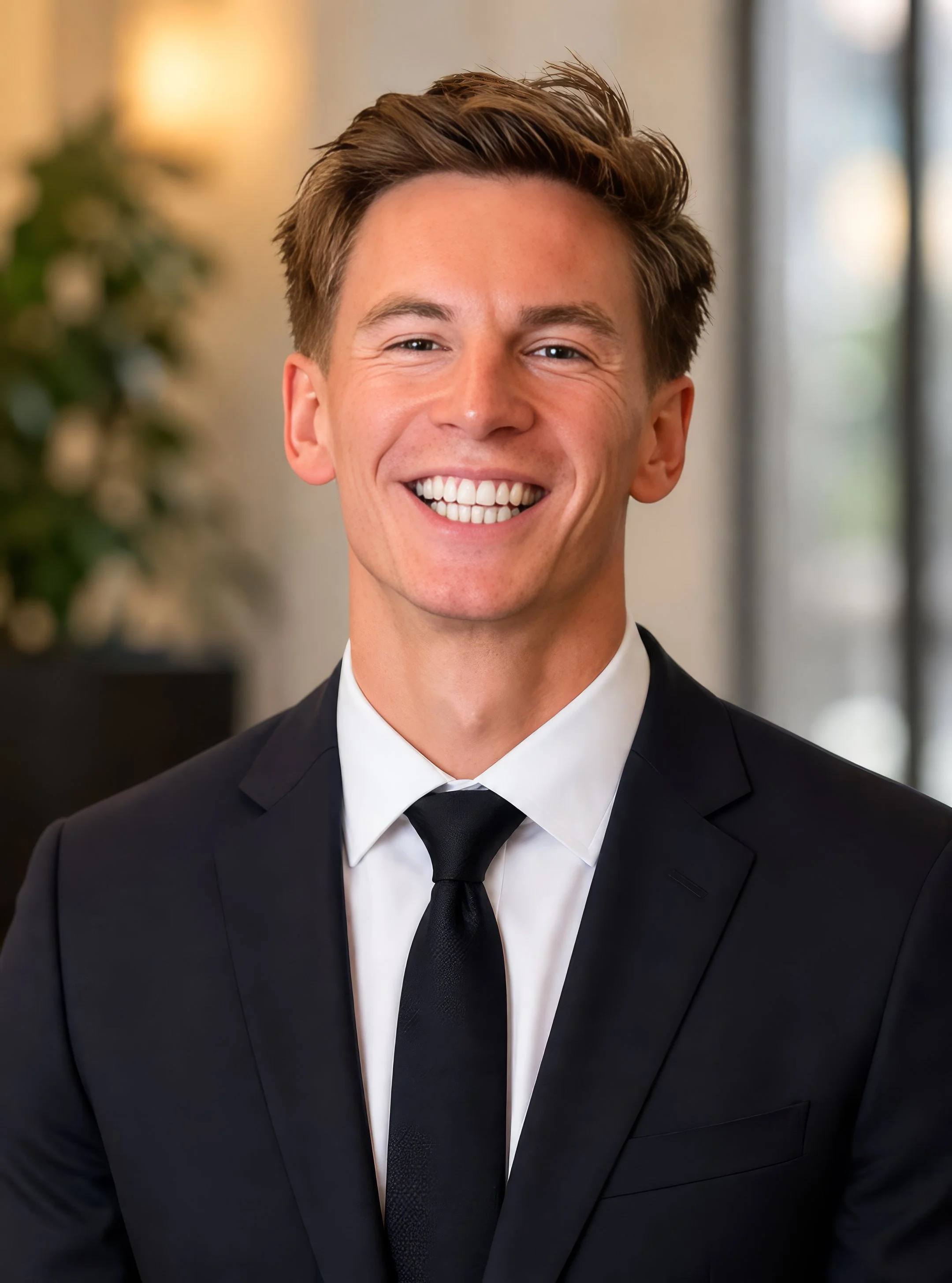 Dr Bradley Powell headshot, smiling young professional man in a smart suit