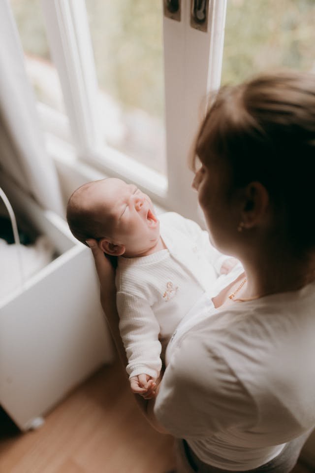 a mother holding a newborn baby infant by a window in a light and spacious room
