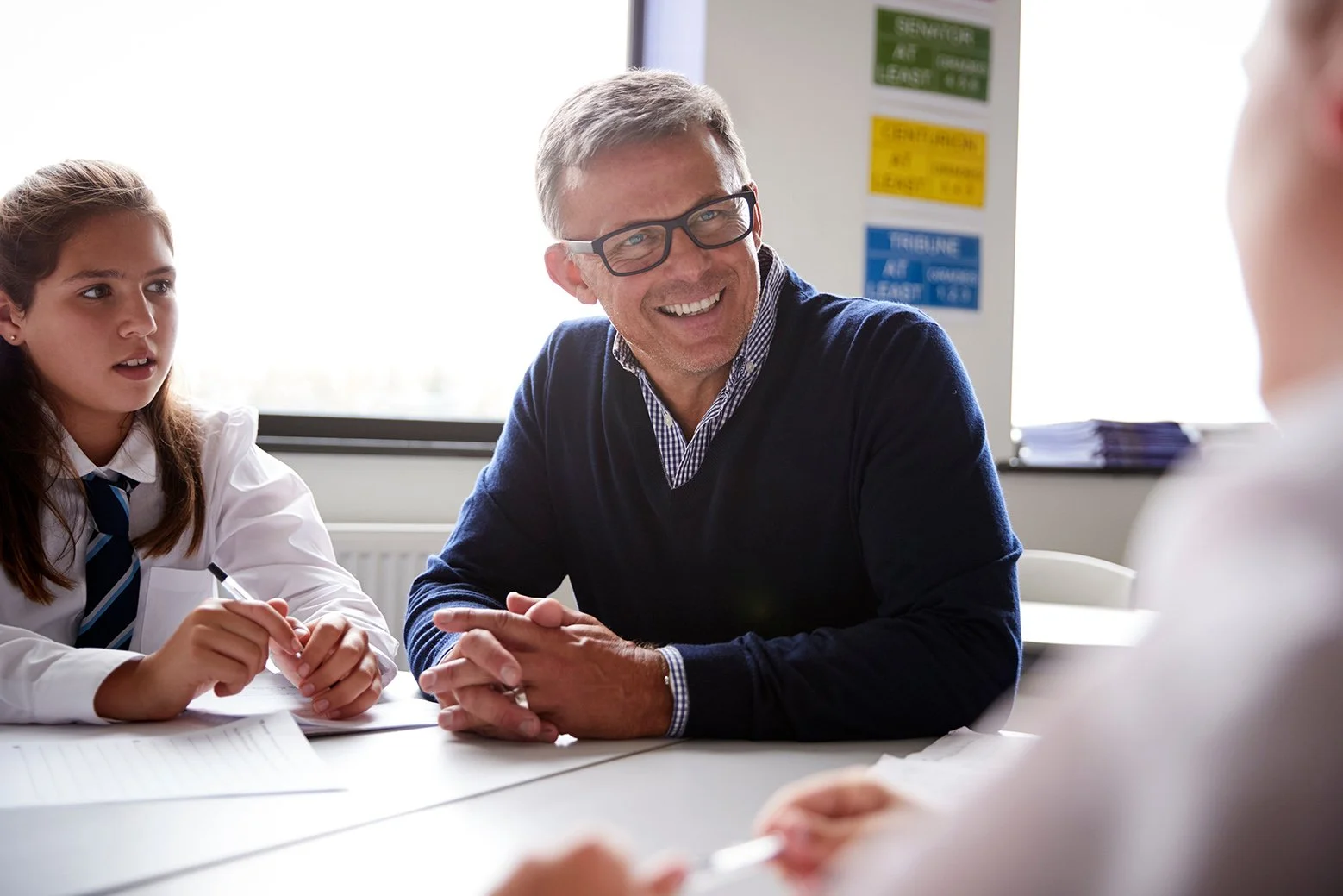 Male High School Tutor Sitting At Table With Students Teaching Lesson