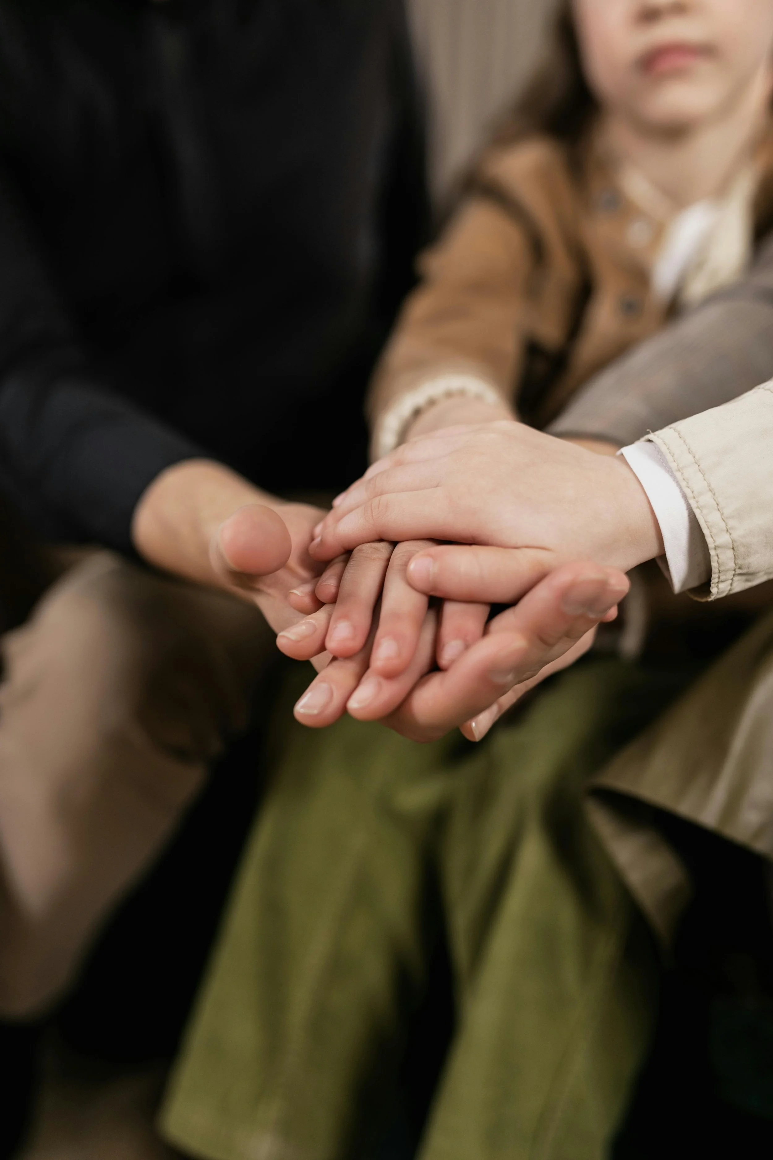 Close-up of two adults and child holding hands together.