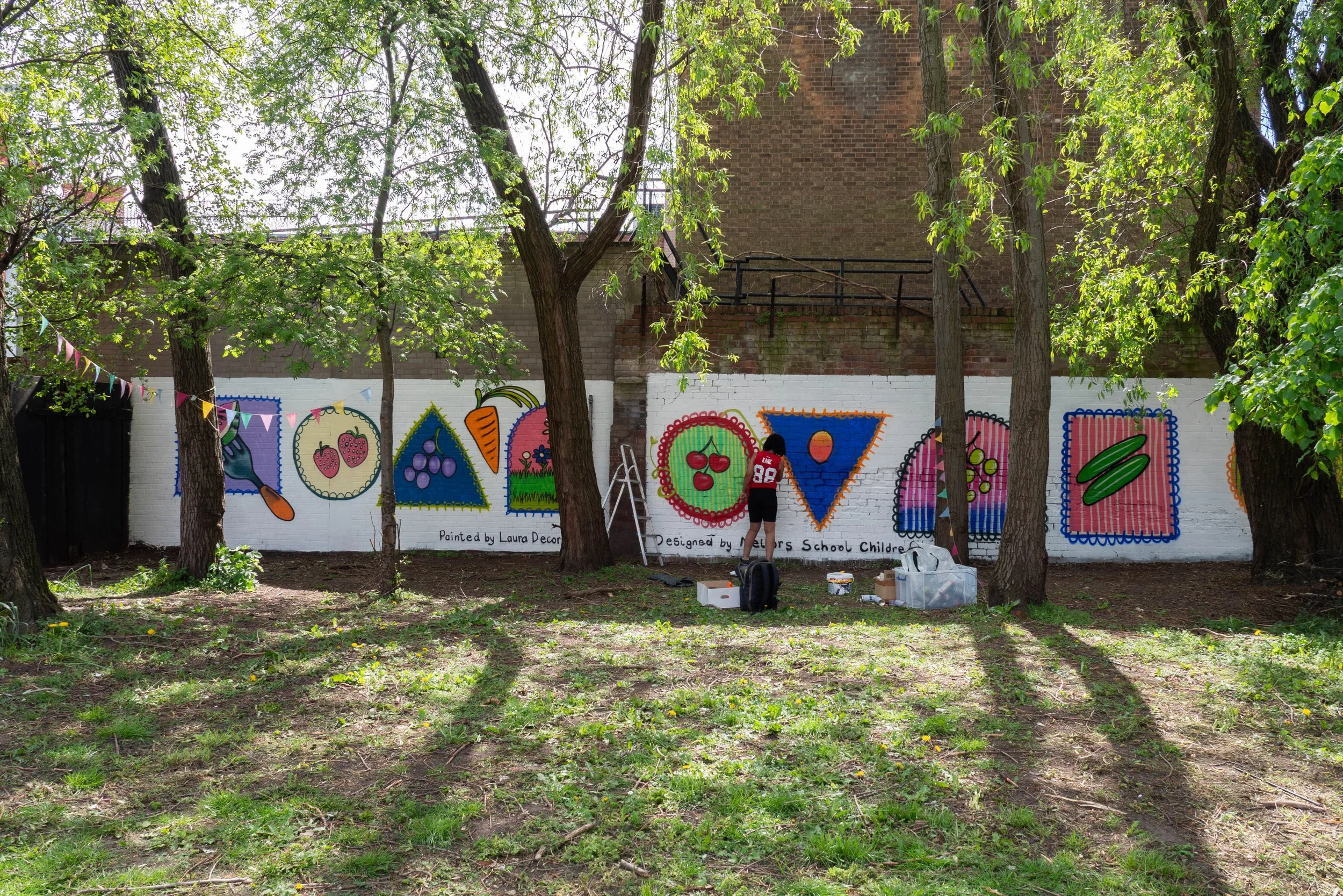 Person painting a mural featuring fruit and vegetables. 