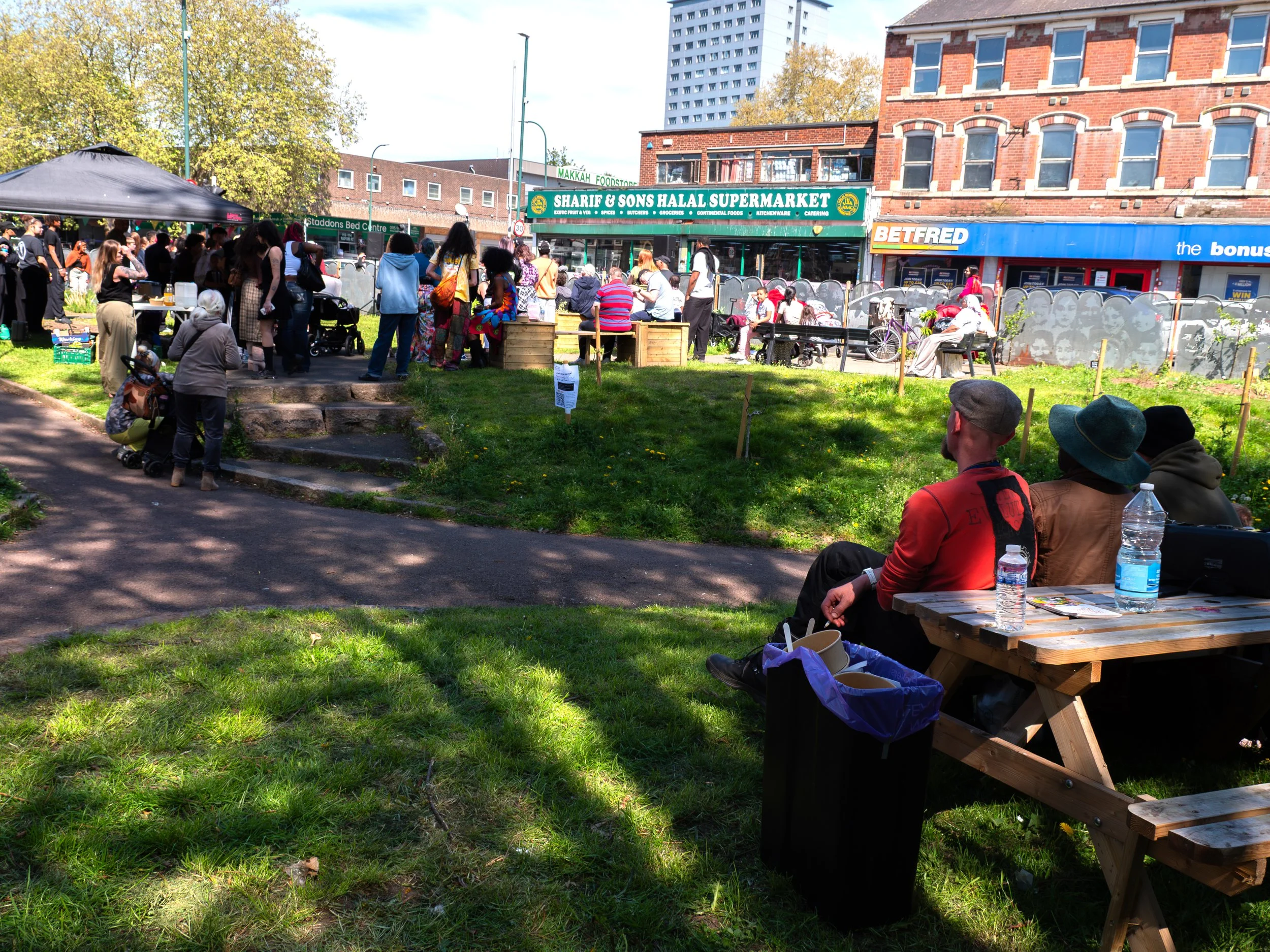 People at a bench in the foreground with crowds around stalls in the background. 