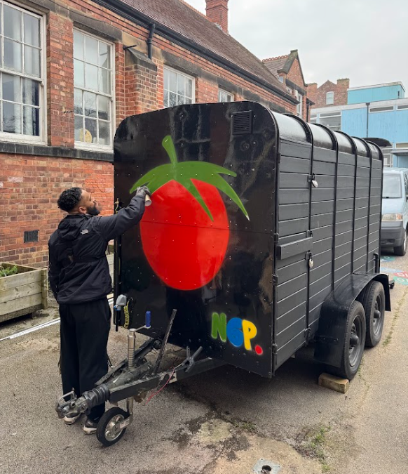 Person spray-painting the image of a tomato onto the side of a food truck.