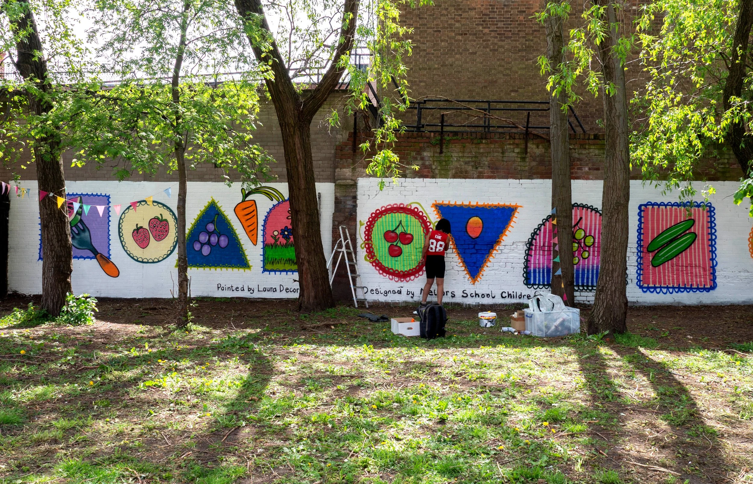 A person painting a mural featuring fruit and veg. 