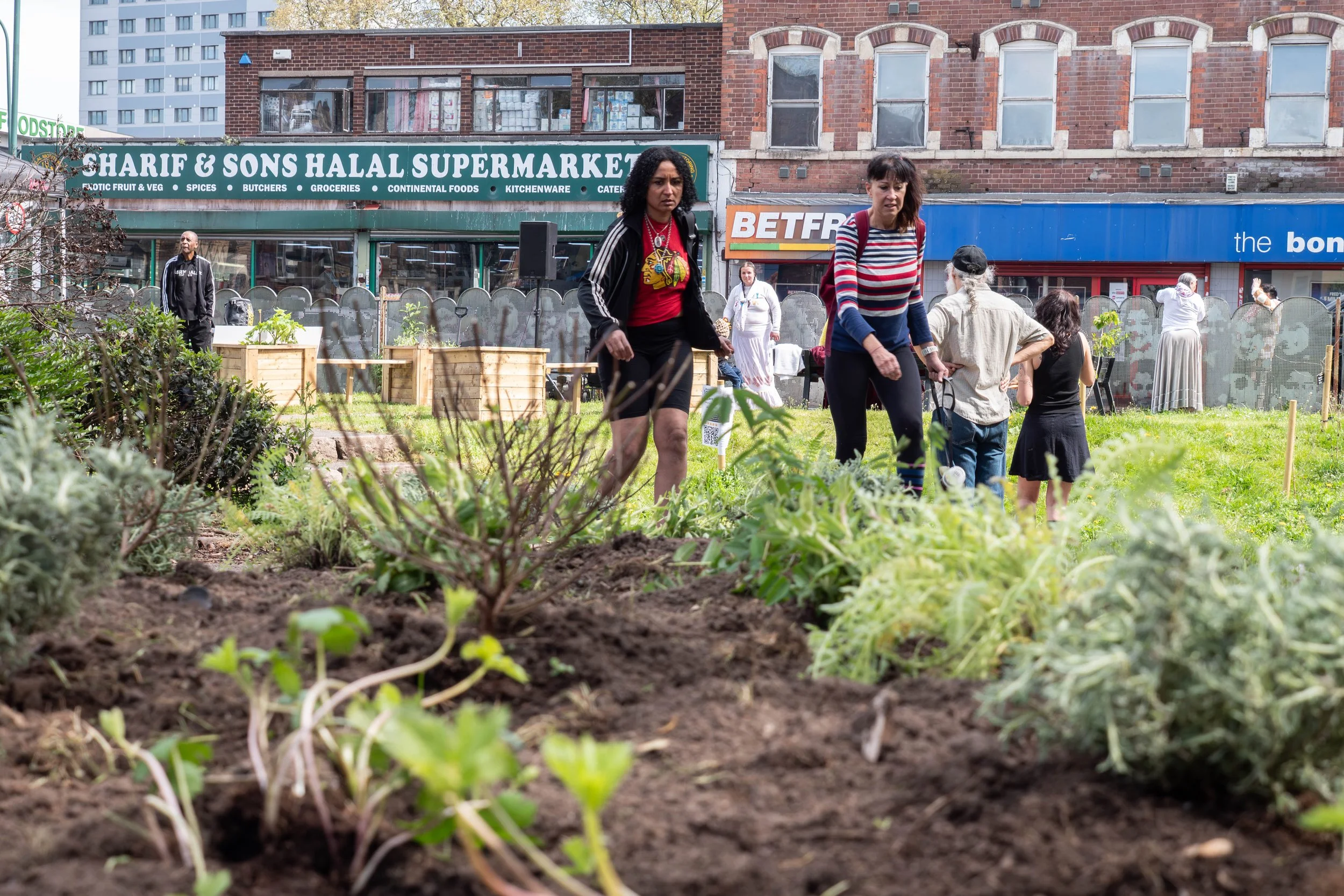 Two people walking past a freshly planted garden bed. 
