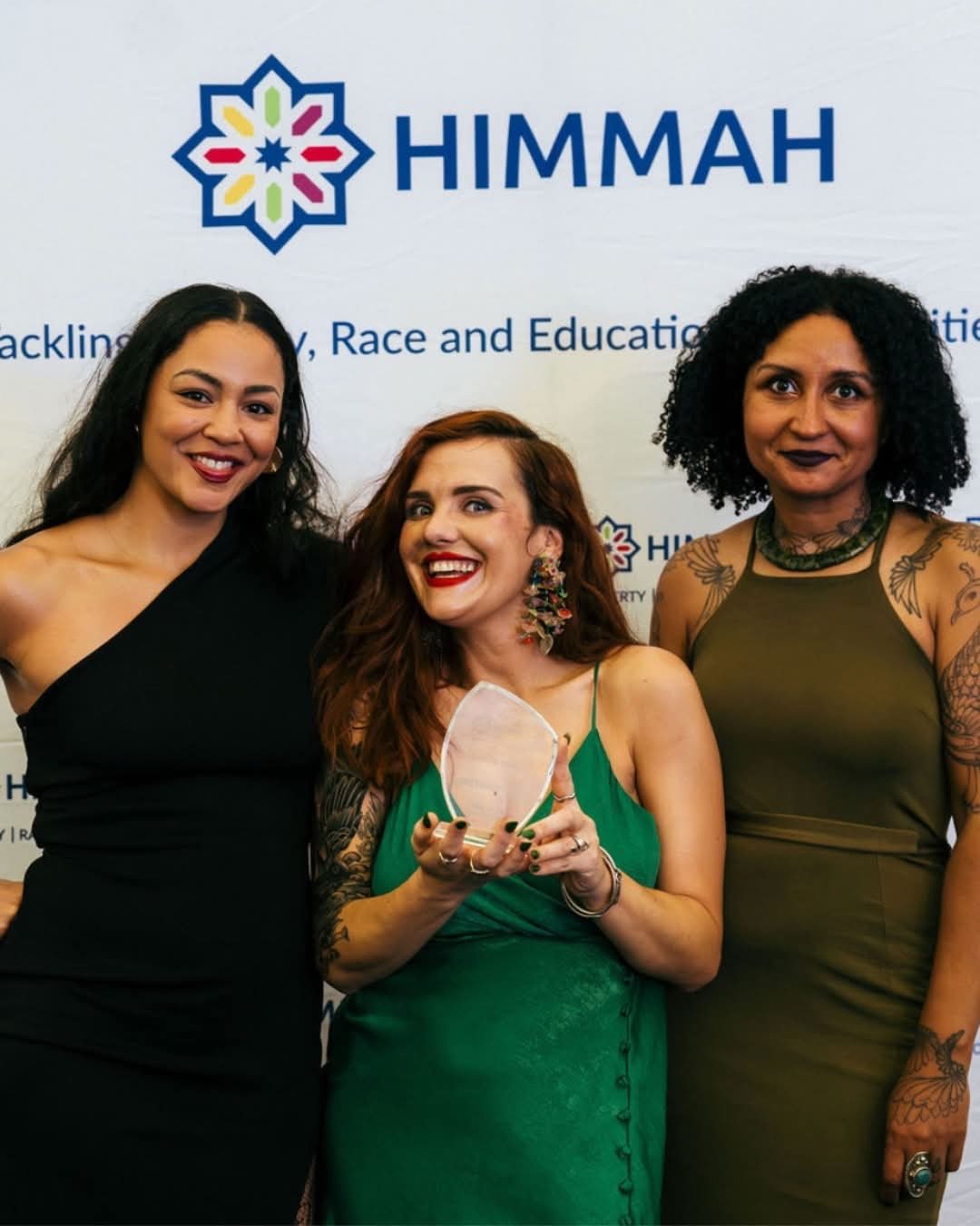 Three women in posh frocks holding a trophy in front of a Himmah sign.