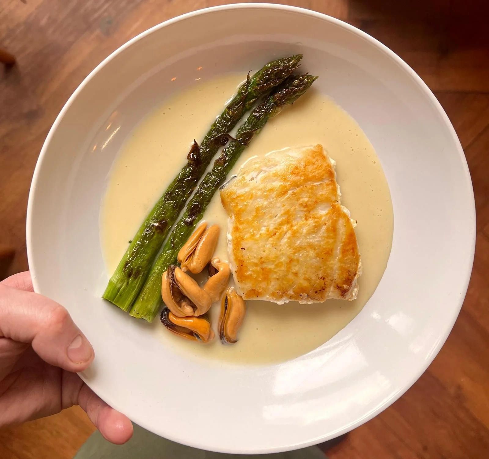 Cooked fish with asparagus and mussels in a white sauce in a round bowl