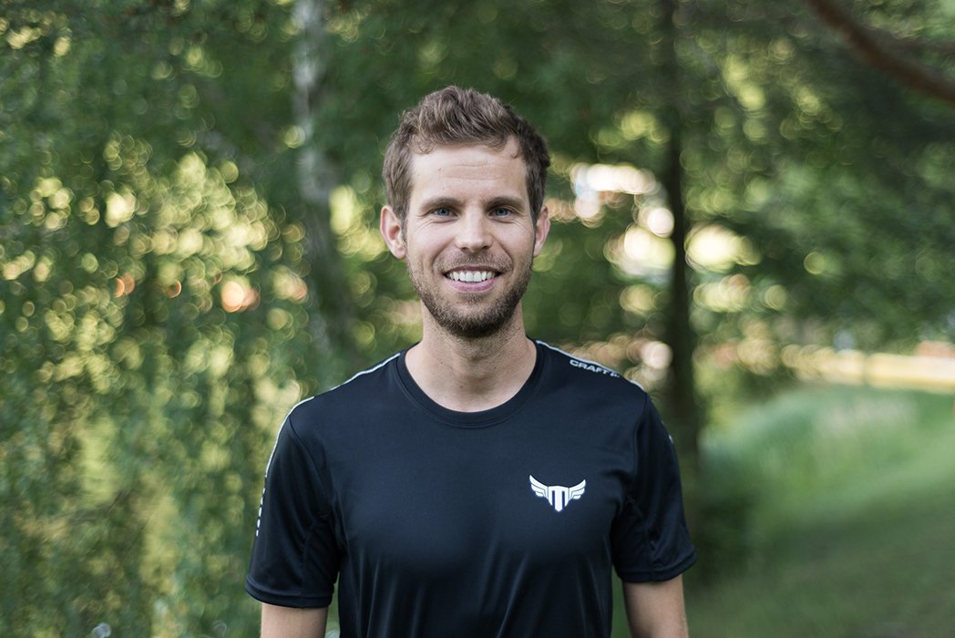 Smiling man in black athletic shirt outdoors in a park.