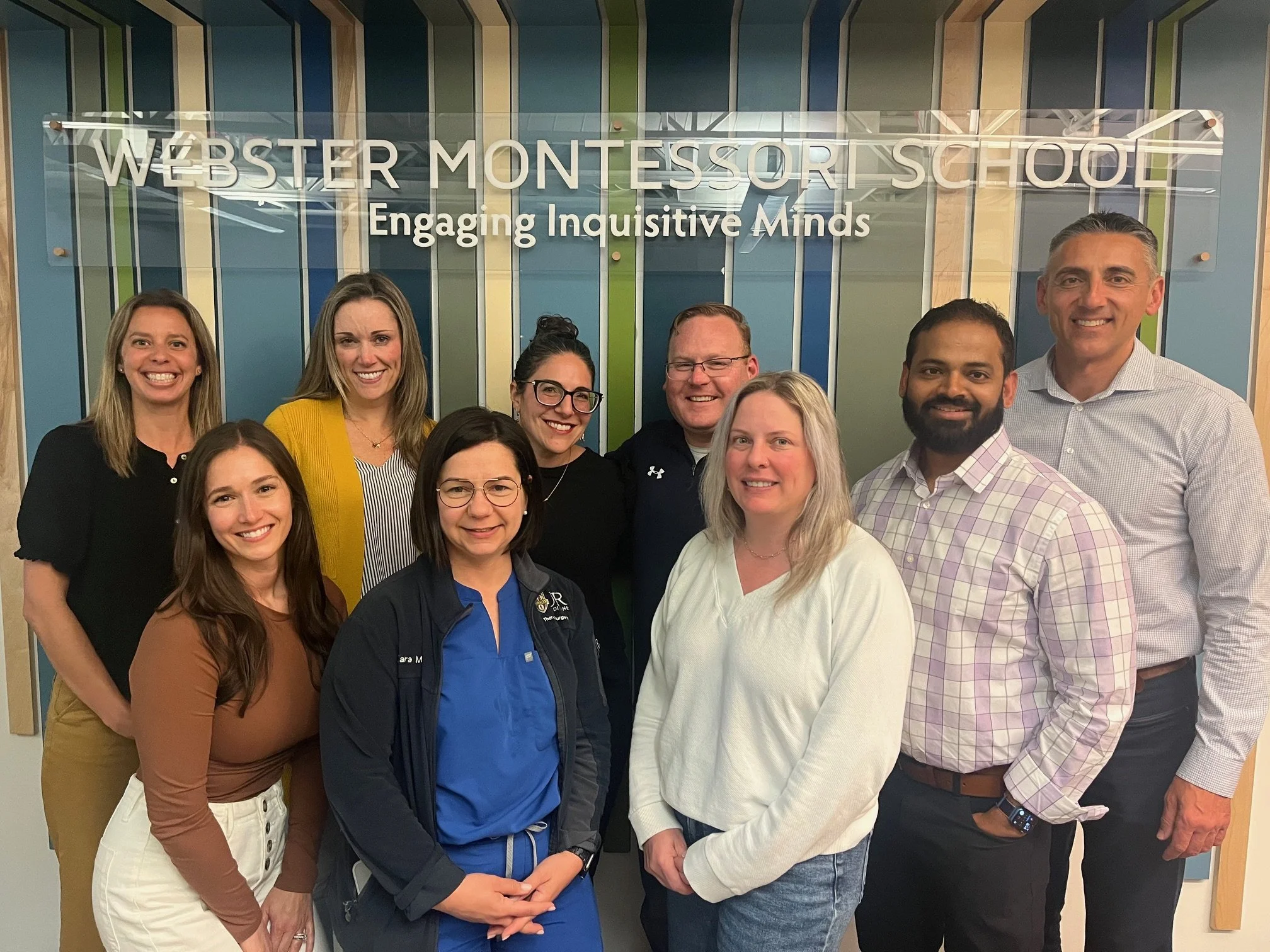 Webster Montessori School Board smiling in front of school sign.