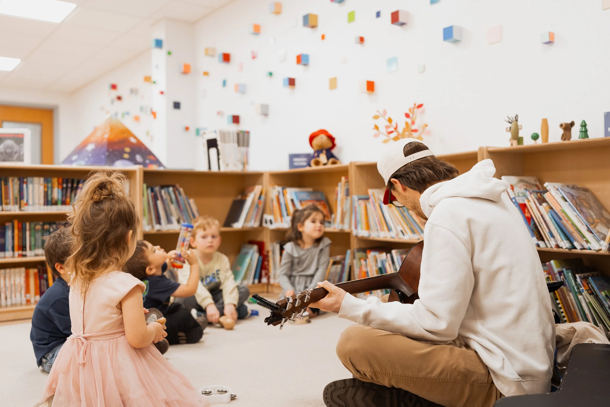 Students sit in a circle with teacher playing guitar.