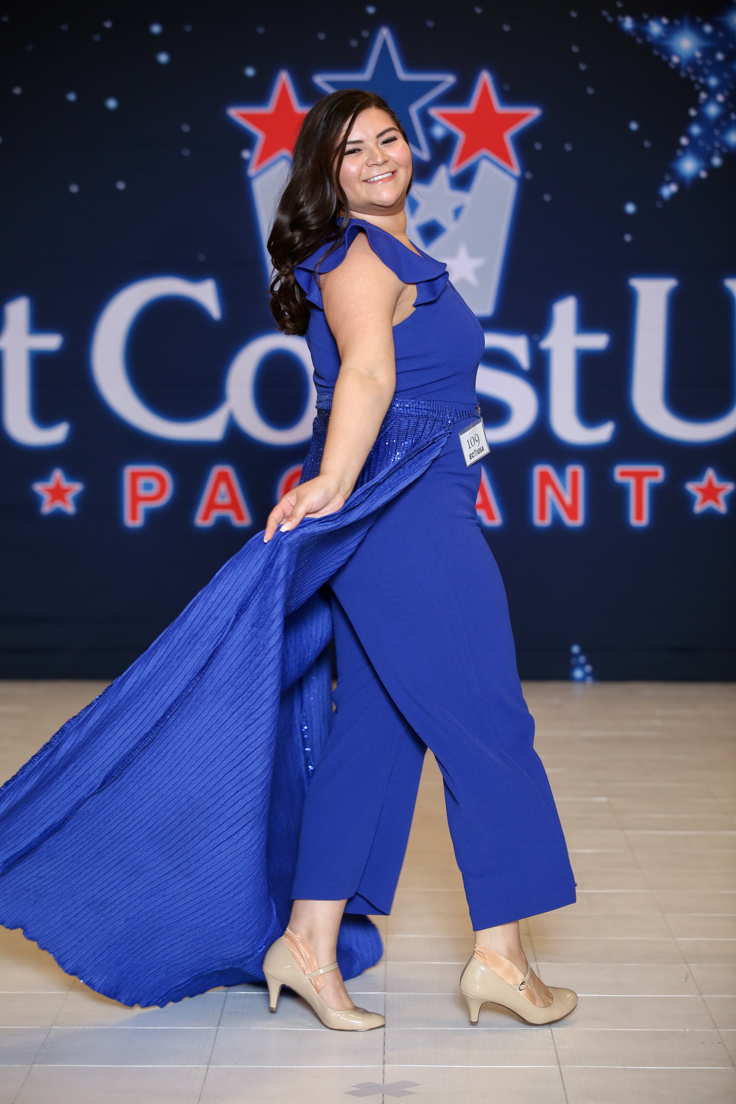 Sonia Yamilex Mata at the 2021 East Coast USA New York Preliminary Pageant during runway competition. She is wearing a blue jumpsuit with a sequin overskirt.