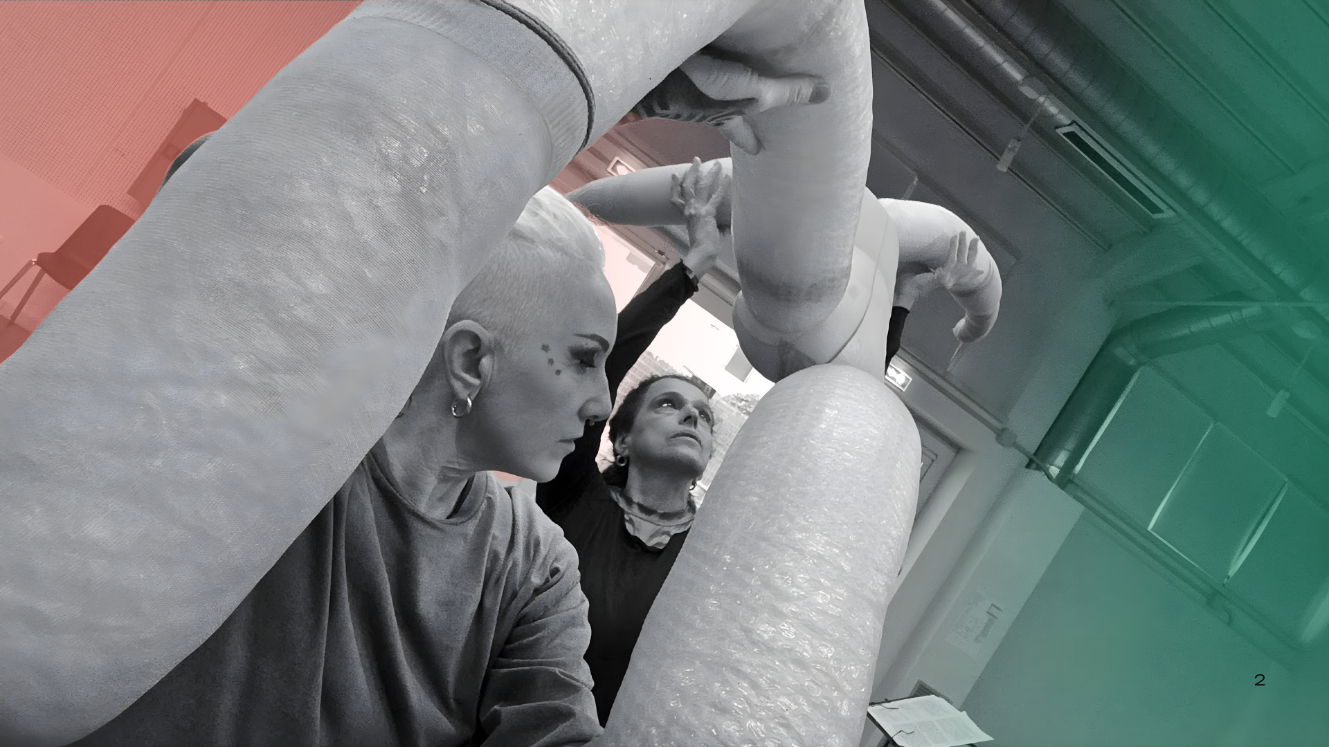 Due donne lavorano su una scultura a forma di figura umana, una più vicina alla telecamera con i capelli molto corti e un'altra più lontana con i capelli raccolti, entrambe concentrarsi sul lavoro.