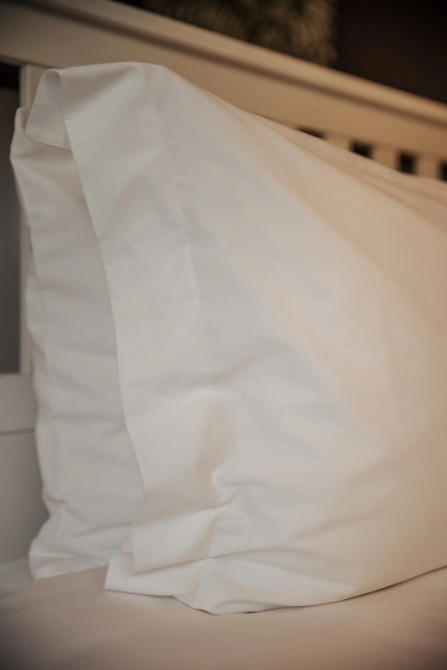Close-up of a white pillow on a bed with a wooden headboard in the background.