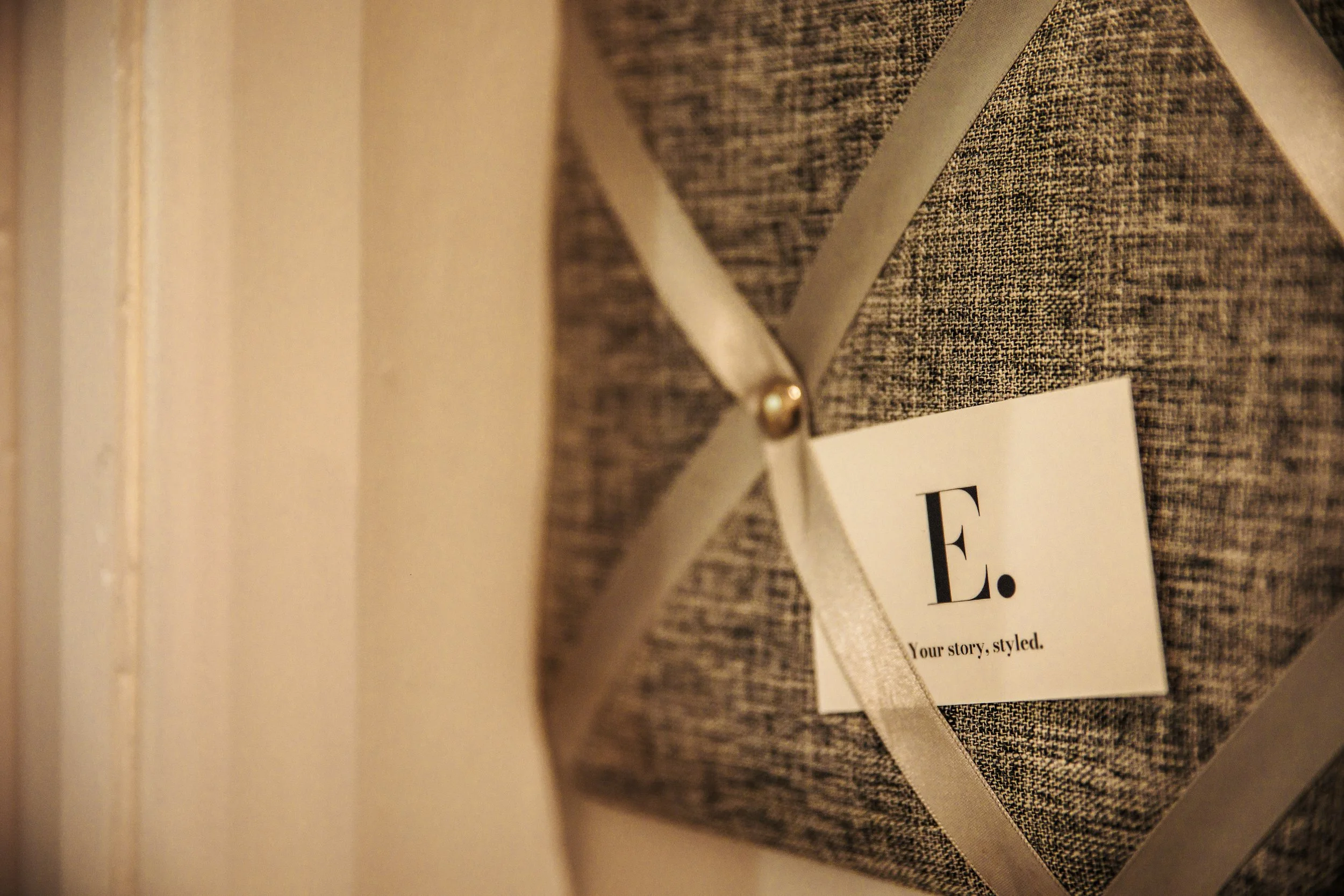 A fabric-covered item with a ribbon bow and a white label reading 'E.' and 'Your story, styled.'