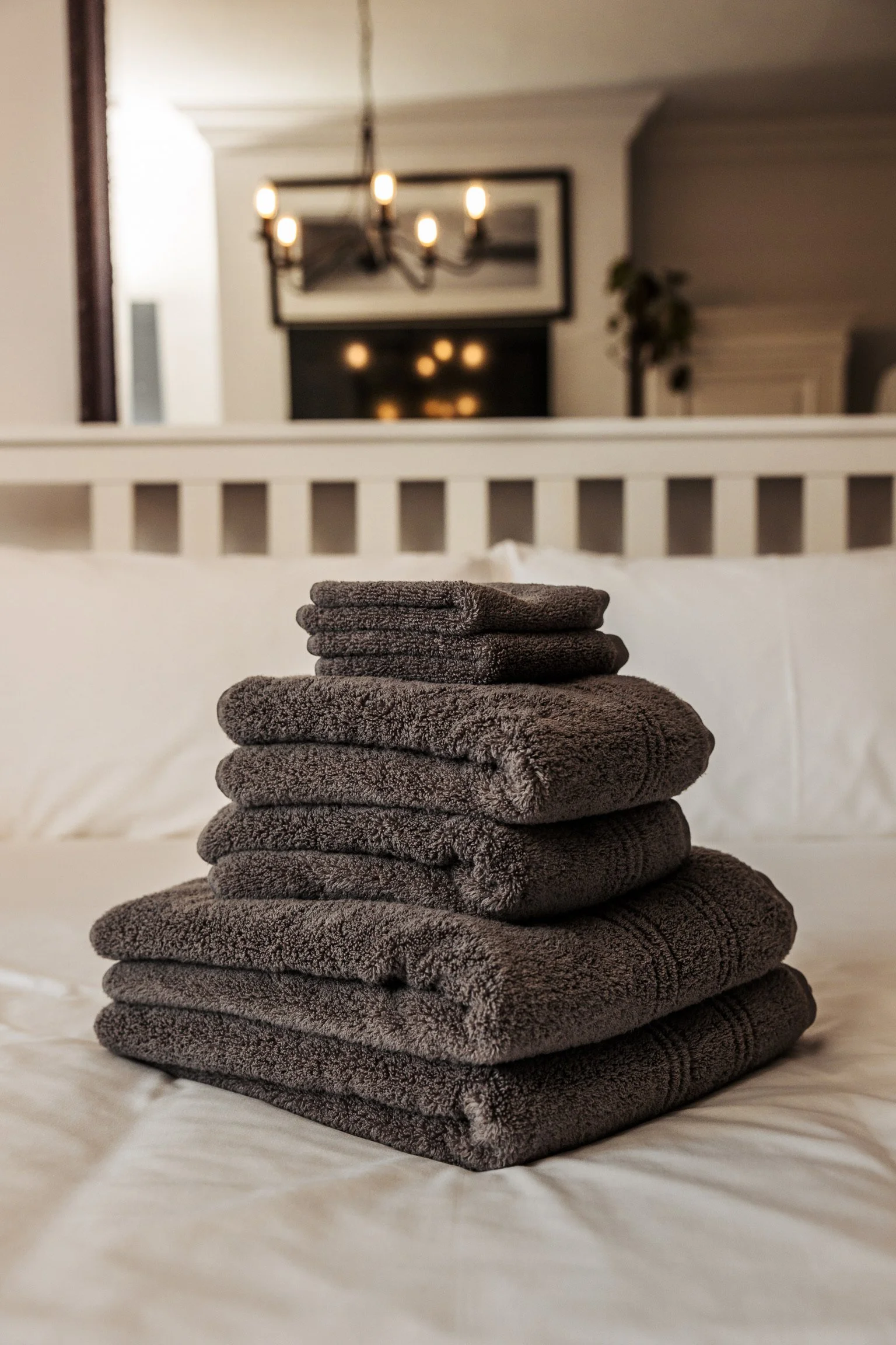 Stacked folded dark gray towels on a white bed.