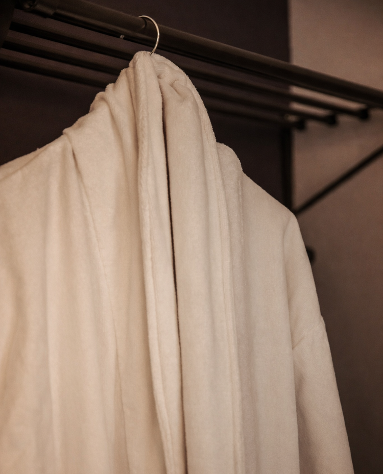 Cream-colored coat hanging on a metal hanger inside a closet.