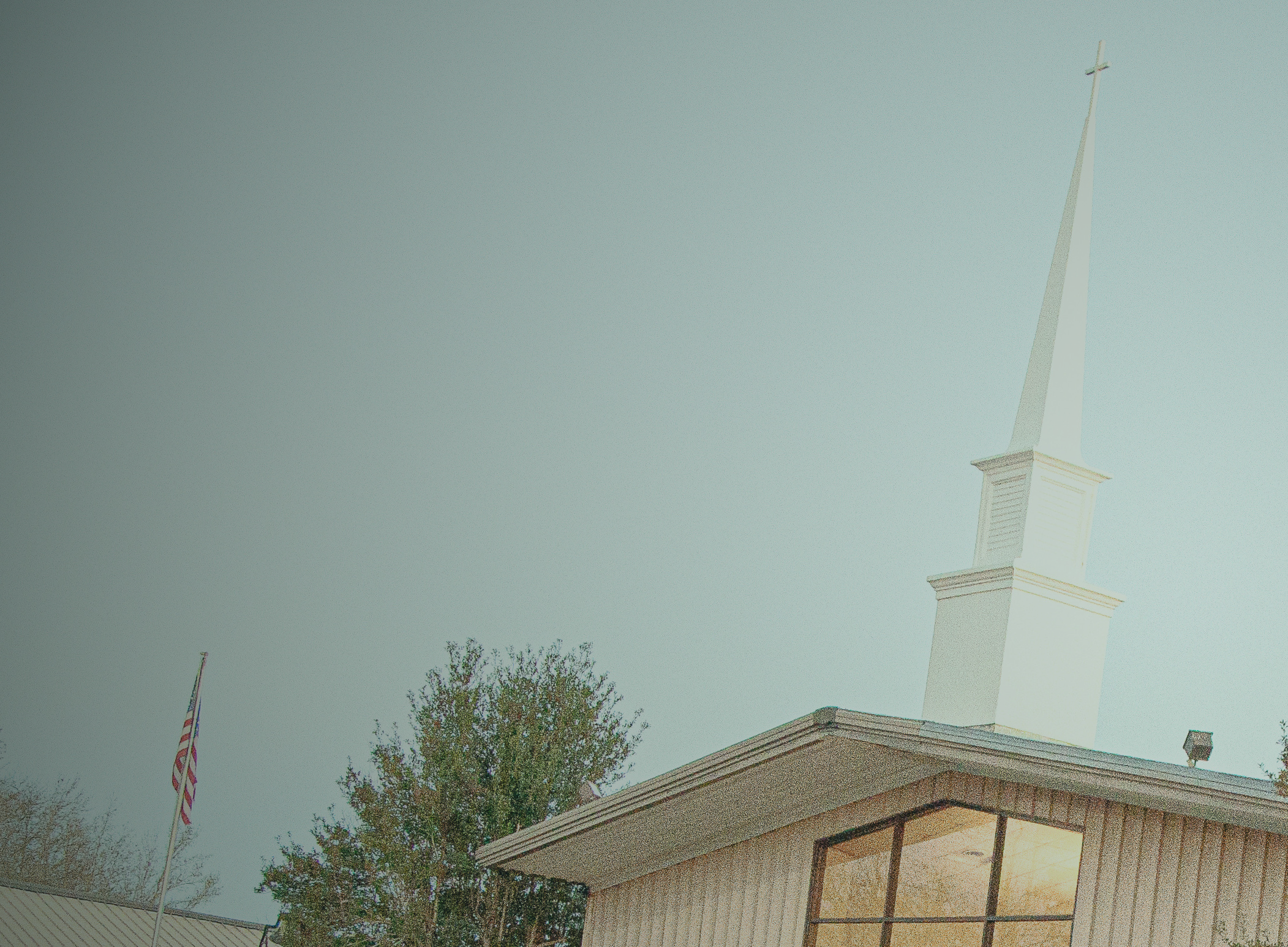 Sweet Springs Baptist Church steeple against a cloudy sky, with an American flag and a tree in the foreground.