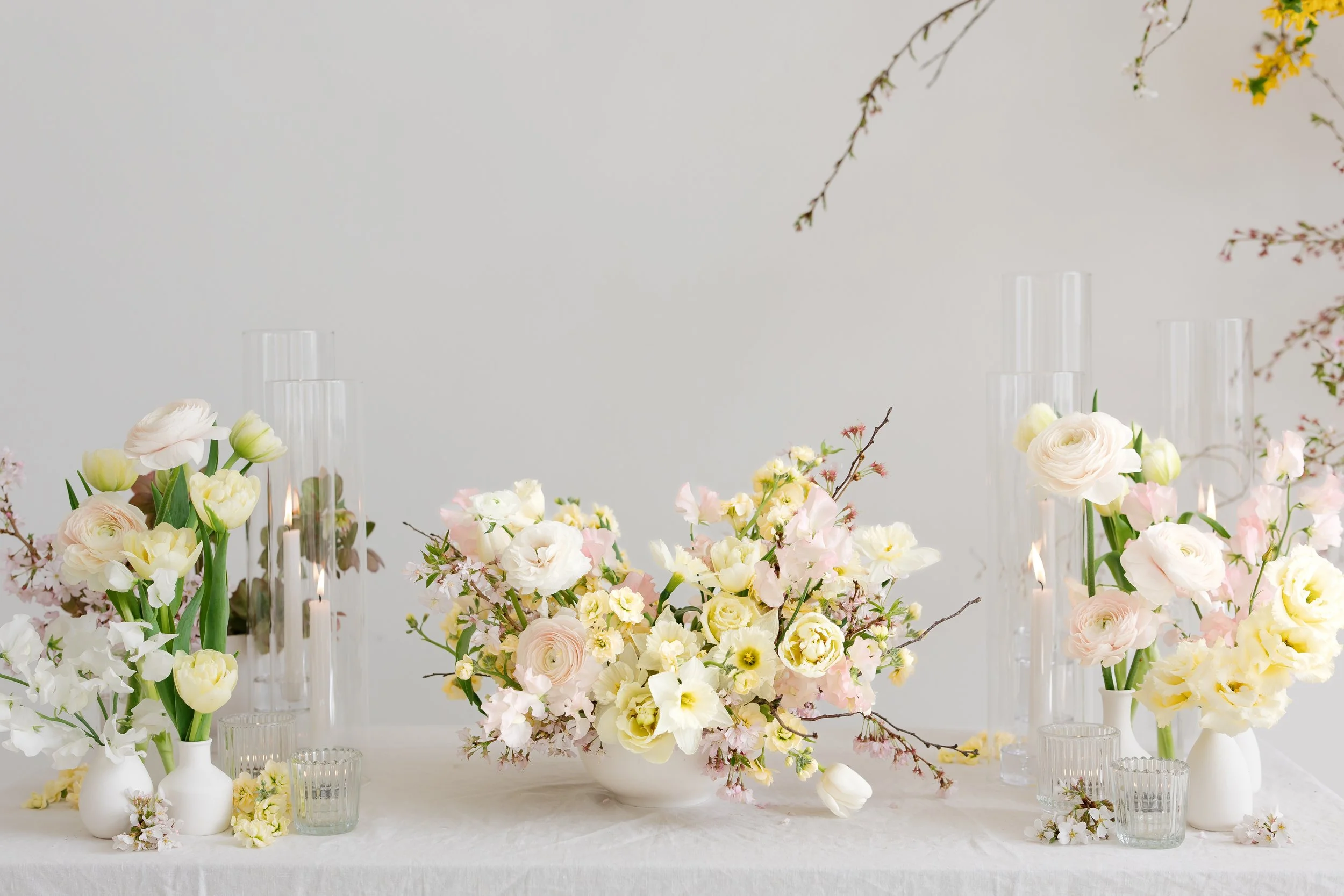 Elegant floral arrangement with white, cream, pink, and light green flowers in white vases on a table, with tall glass candle holders in the background in Buffalo, NY for a corporate function.