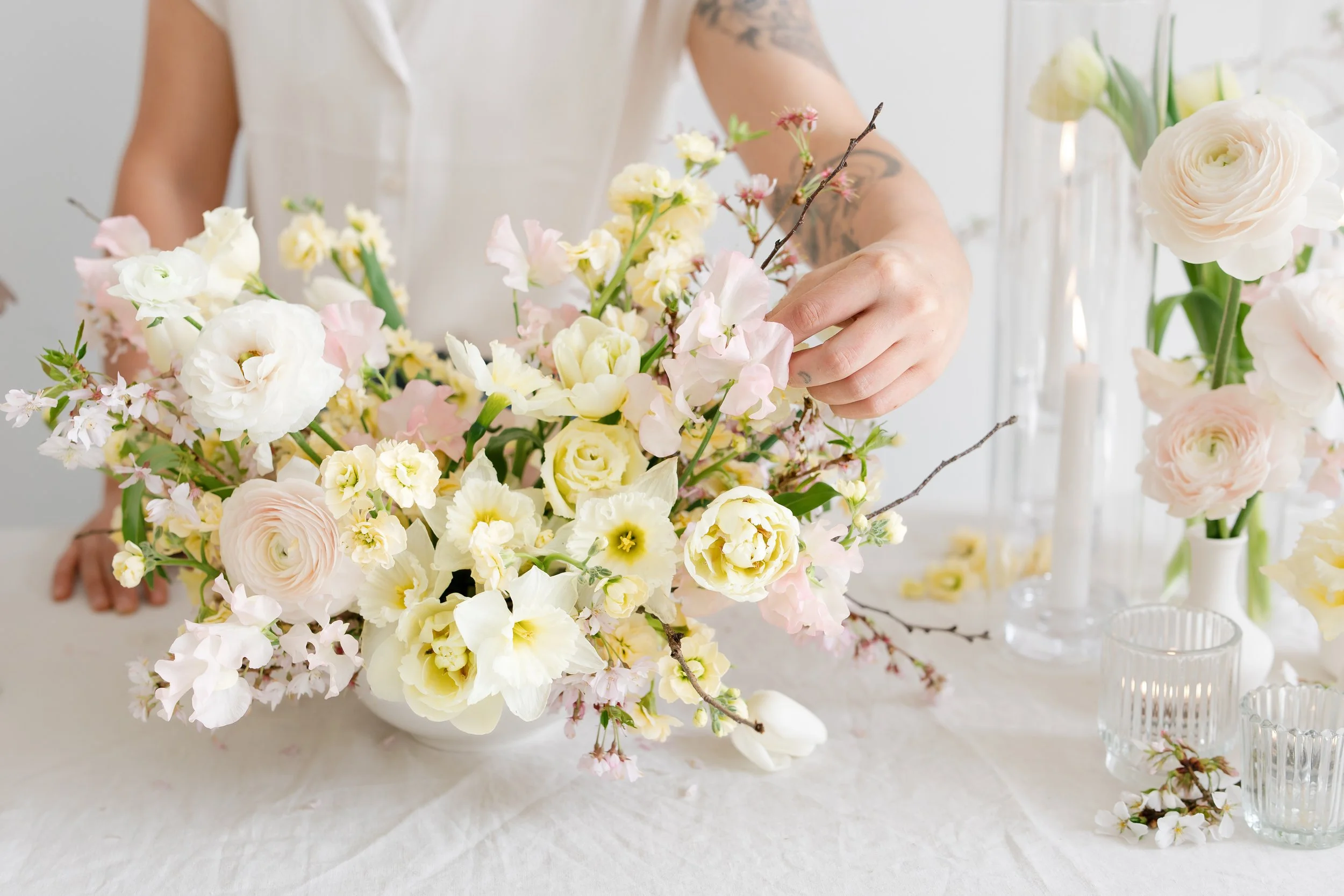Close-up of a person arranging a large spring, pastel-colored flower arrangement for a luxury wedding, with glass candle ware in the background.