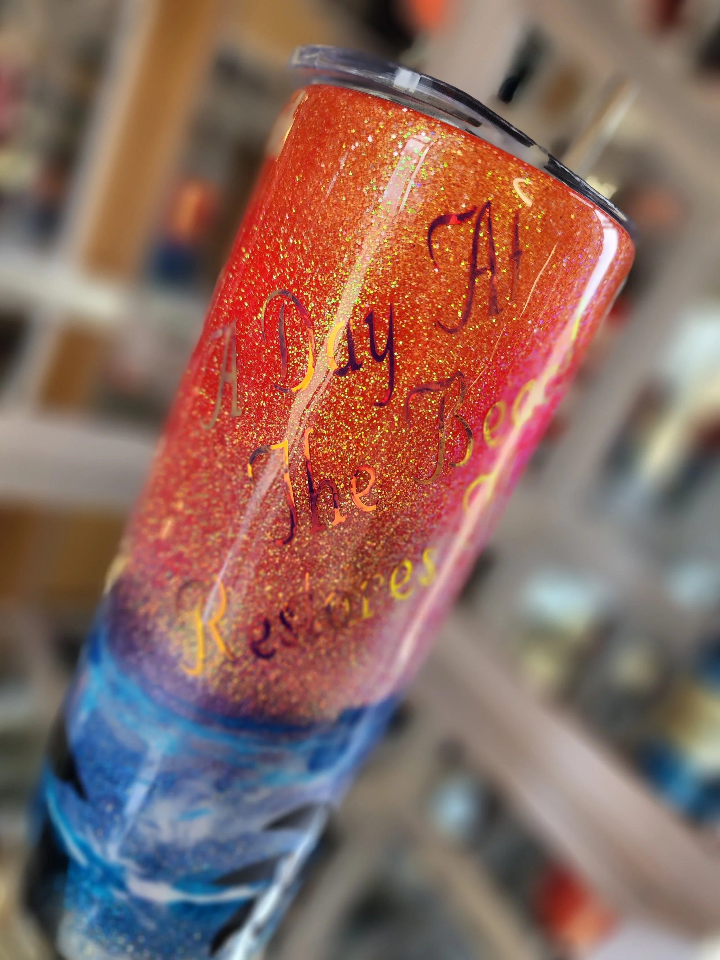 Close-up of a glittery tumbler cup with an inspirational quote, featuring red, orange, yellow, and blue colors.