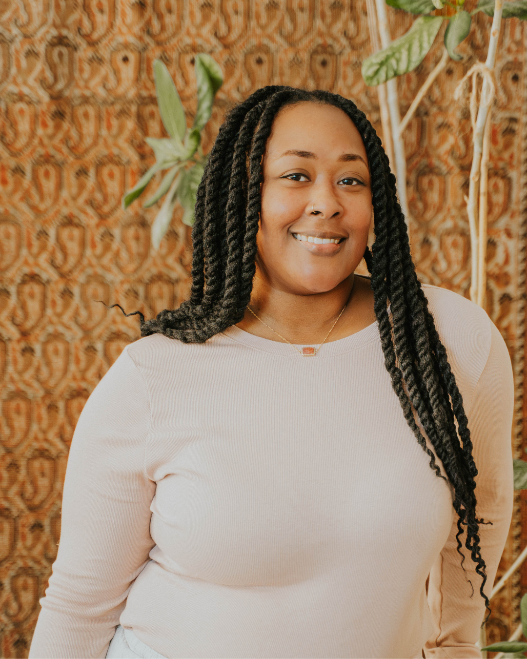 Close-up photo of a woman with dark hair, wearing an orange top, looking at the camera with a slight smile.