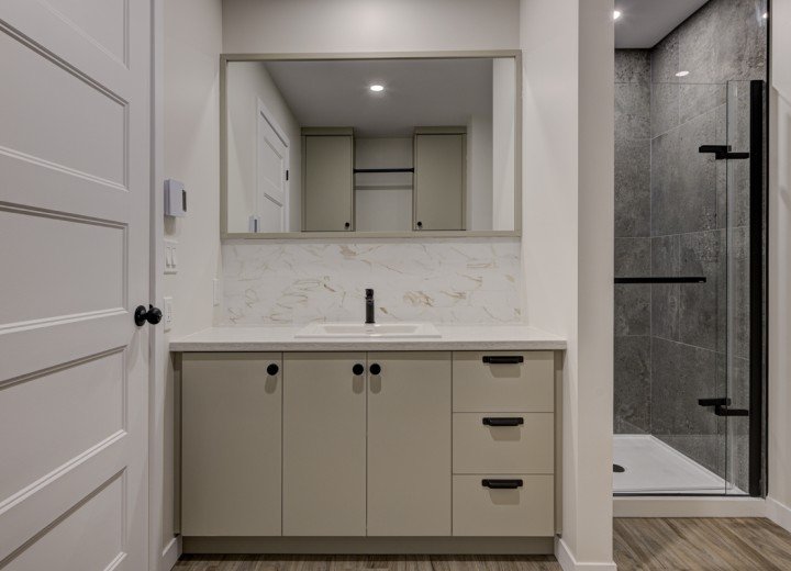 Salle de bain moderne avec lavabo, miroir, armoire et douche vitrée.