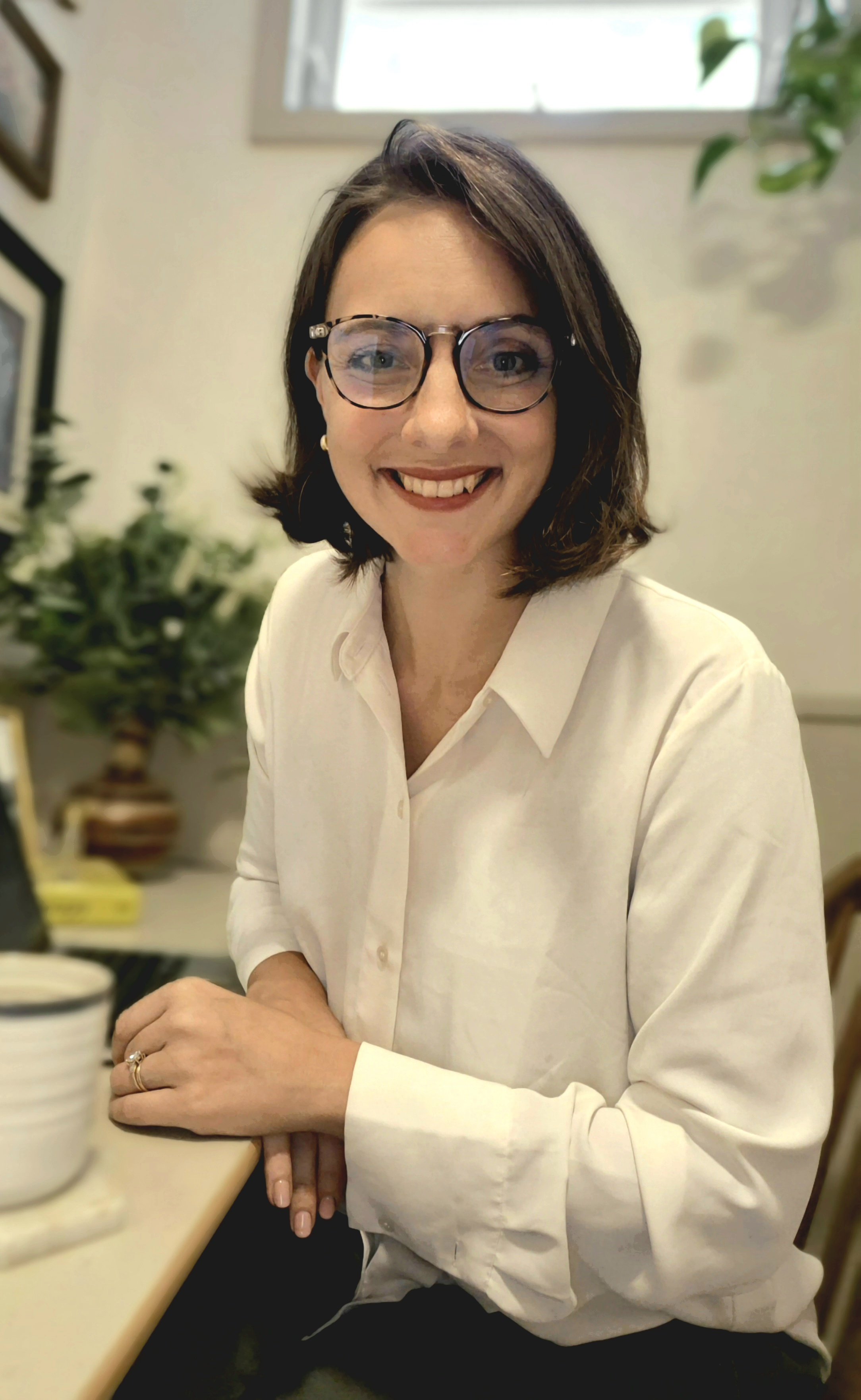 Kia Gutierrez Smiling woman with glasses and brown hair sitting at a table in a cozy indoor setting, wearing a white blouse.