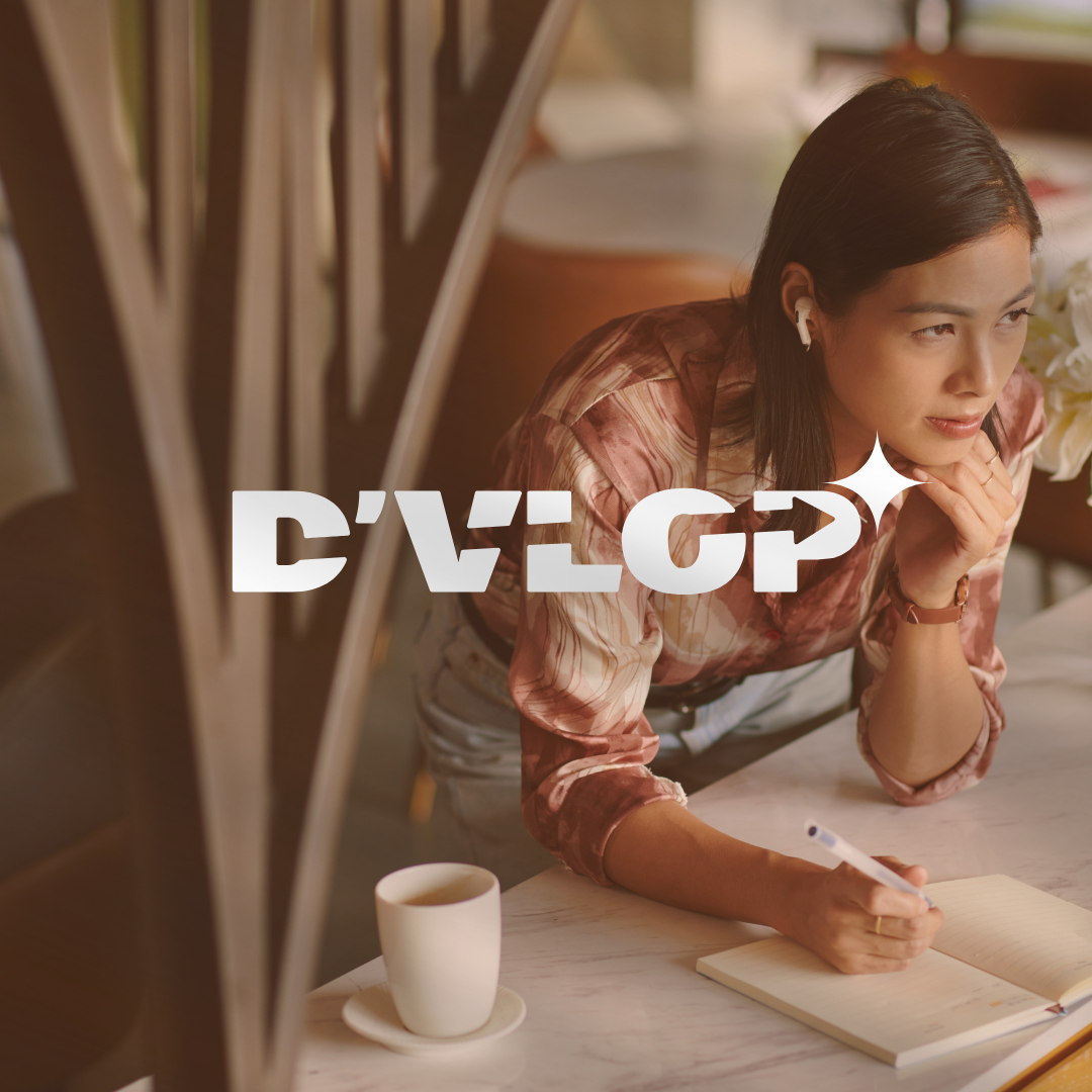 Une femme assise à une table, en train d'écrire dans un carnet, portant des écouteurs sans fil, un mug à côté d'elle.