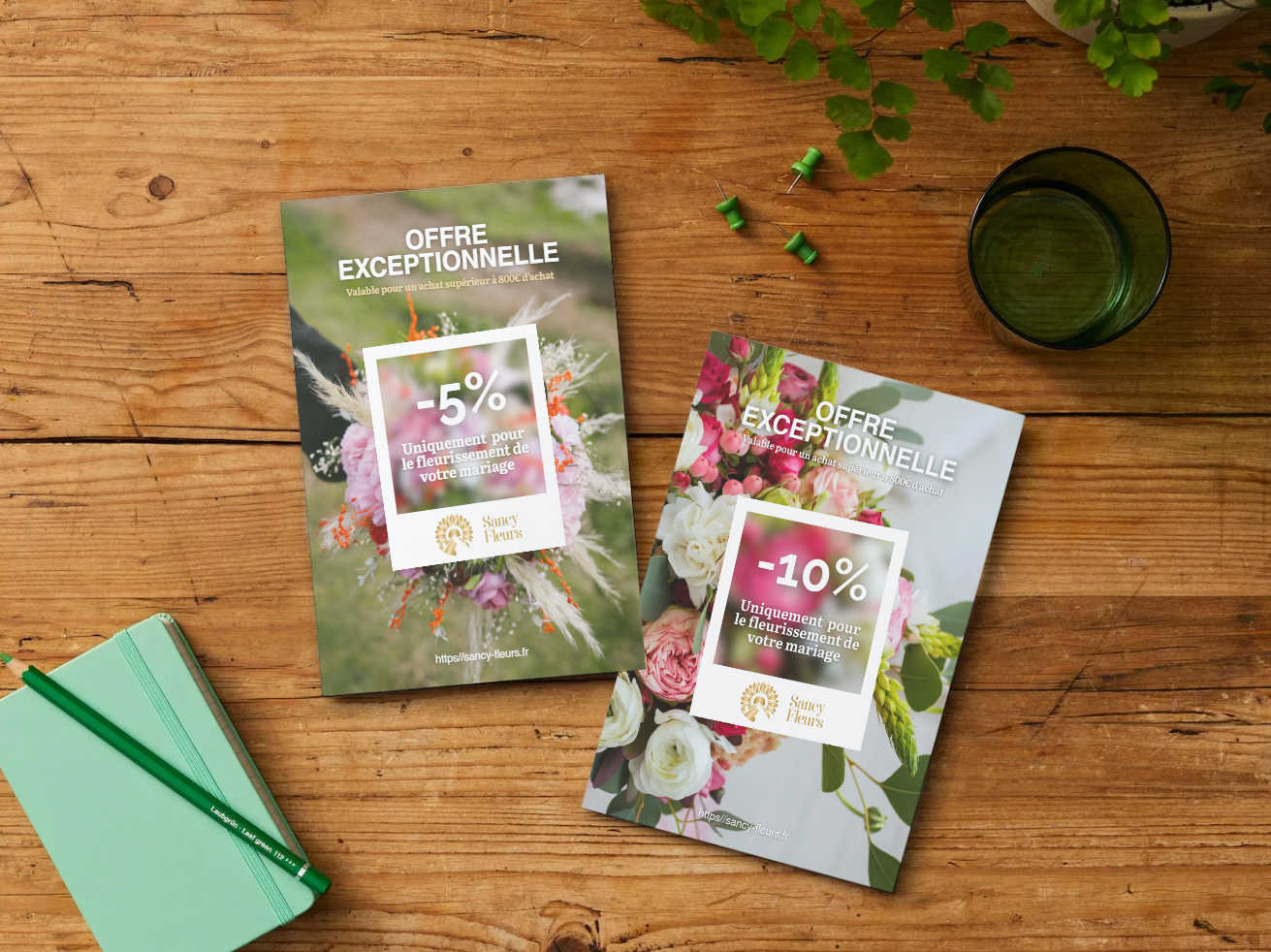 Deux flyers publicitaires pour des offres exceptionnelles sur des fleurs de mariage, affichant des réductions de -5% et -10%, posés sur une table en bois avec un verre transparent, un carnet vert avec un stylo vert, et une plante. Le site web Sancy Fleurs est également visible sur les flyers.