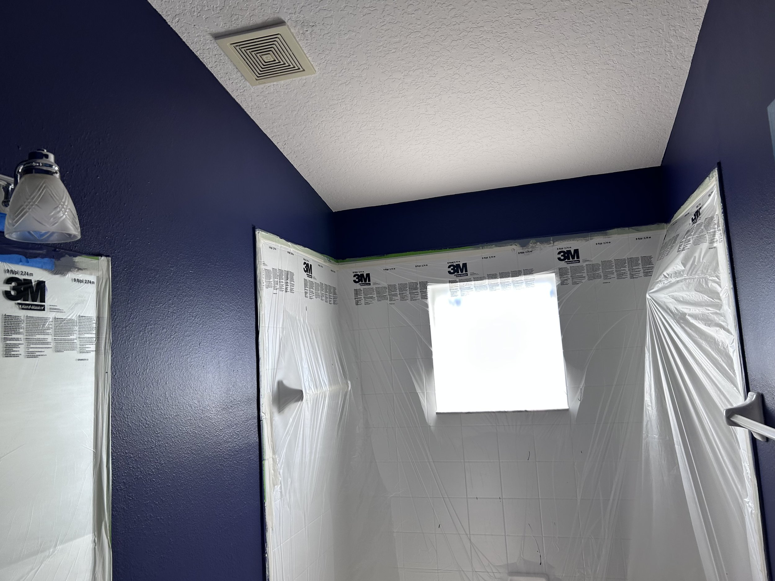 Bathroom with dark blue walls, partially covered white tiles, a small window, and a ceiling light.