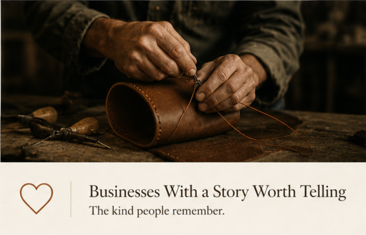 Close-up of a craftsperson's hands sewing leather with a needle and thread, tools on a wooden workbench, and part of a brown leather item.
