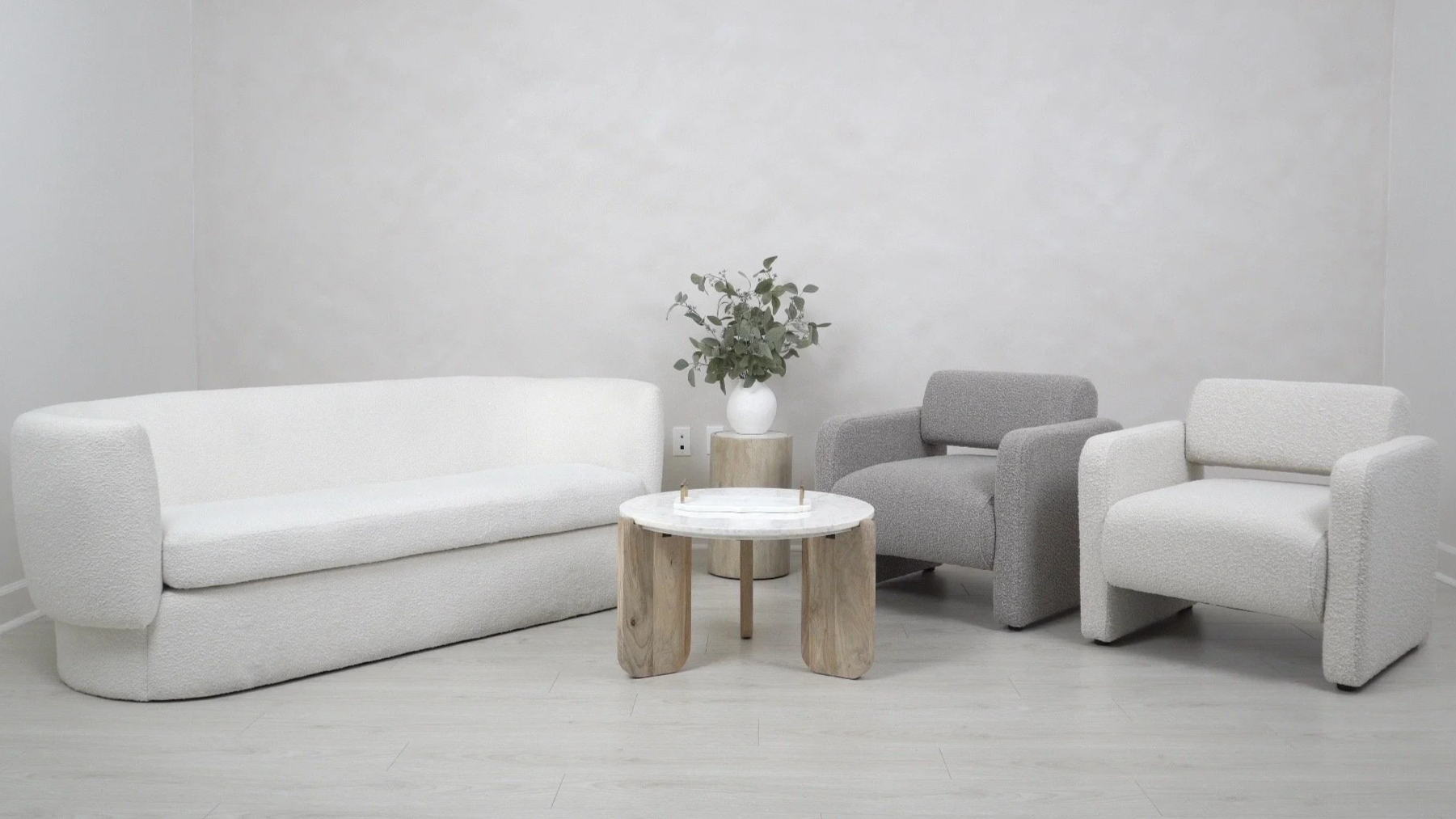 Minimalist living room with a white sofa and two armchairs, a small round marble coffee table, and a potted plant on a wooden pedestal