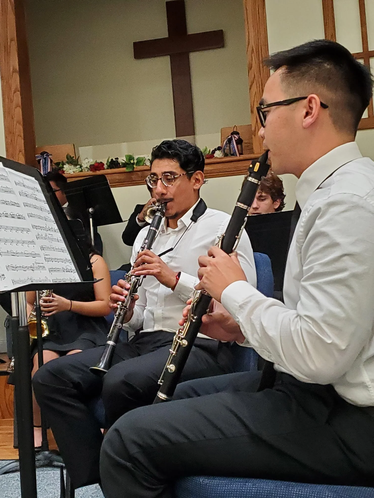 Two musicians playing clarinets during a concert inside a church. A cross is visible on the wall behind them.
