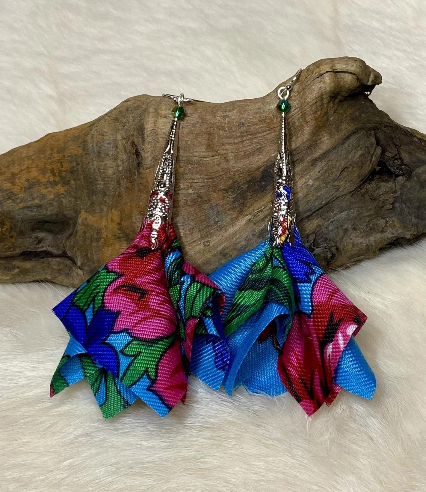 Colorful handcrafted floral fabric earrings with floral pattern and silver hooks, displayed on a piece of driftwood.