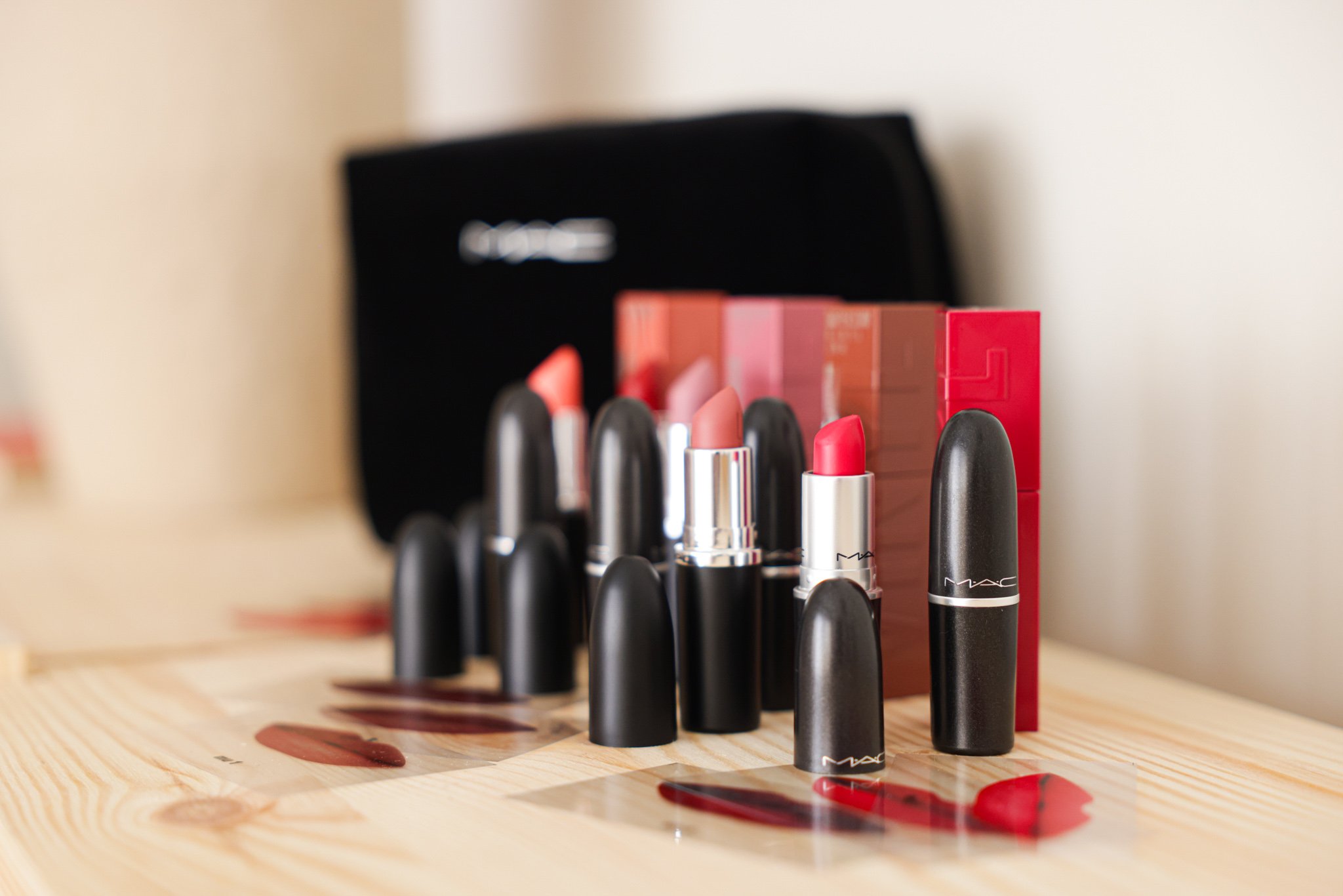 Assorted MAC lipsticks on a wooden surface with a black MAC bag in the background.