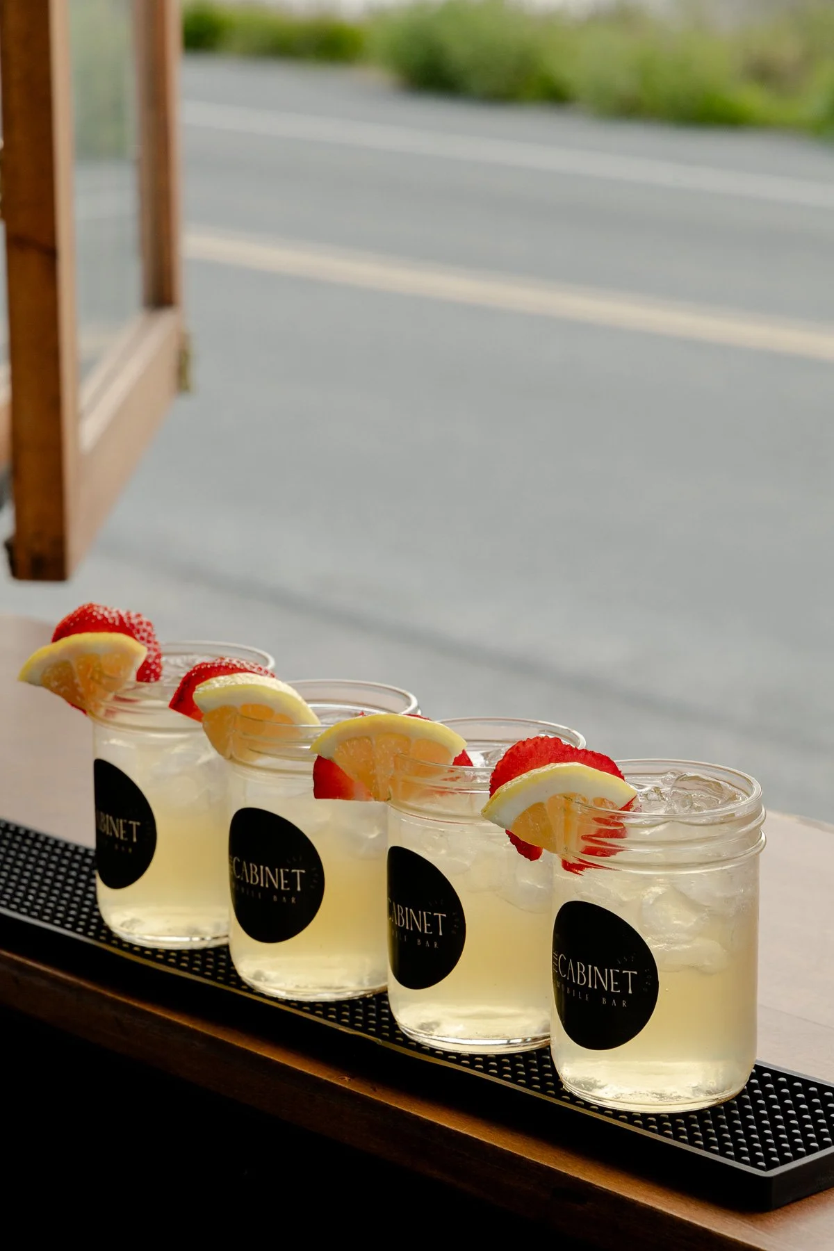 Signature lemonade highballs garnished with strawberry and lemon at an outdoor Vancouver Island wedding bar.