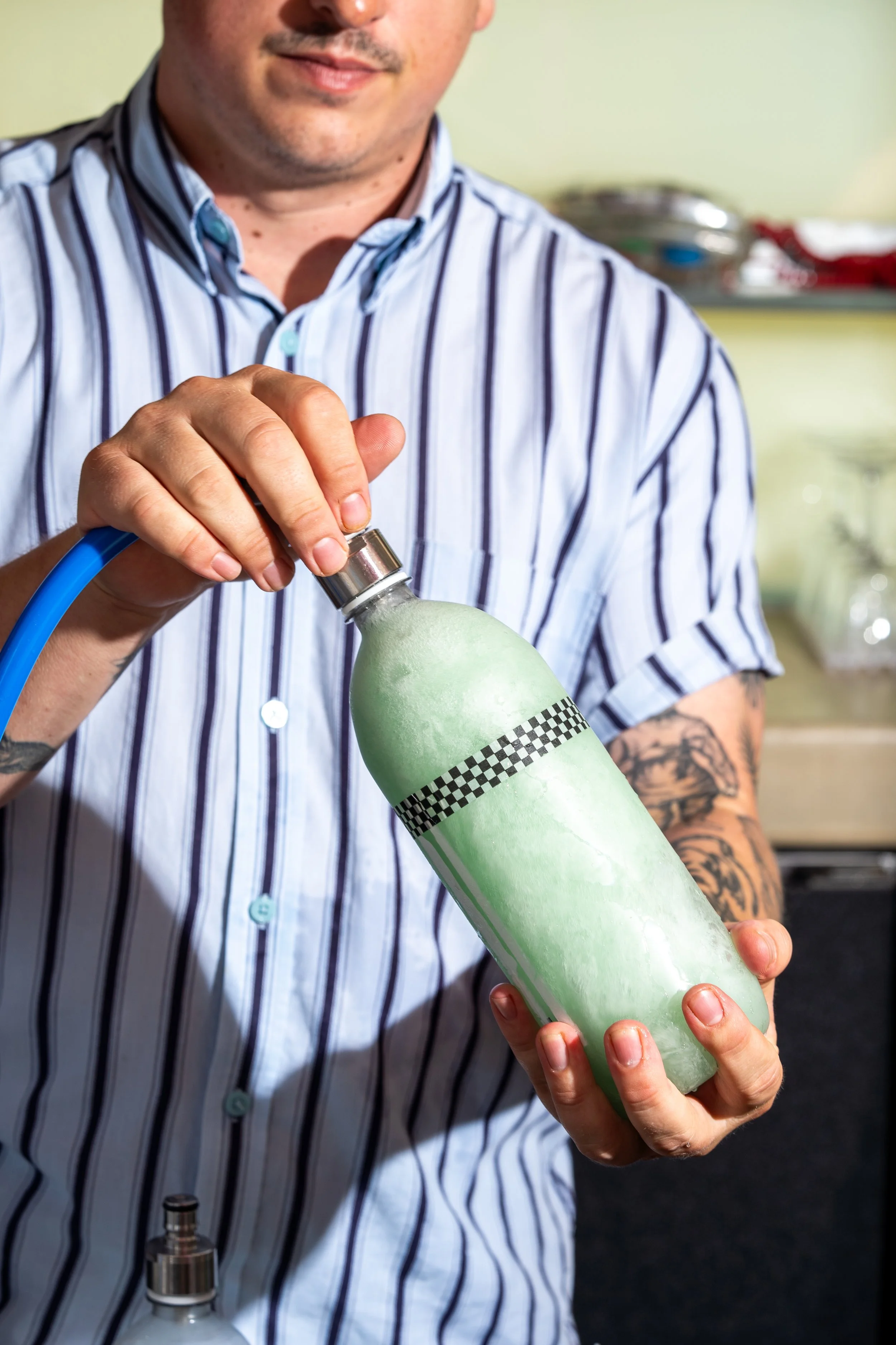 Person in a striped shirt holding a green and white bottle with a black and white ribbon label.