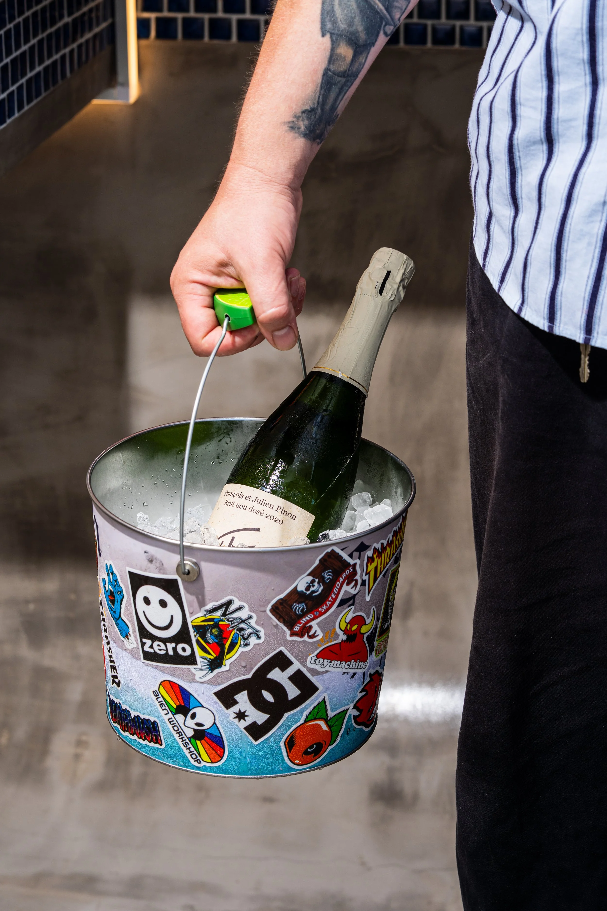 A person holding a bucket decorated with stickers, placing a bottle of champagne in a bucket of ice.