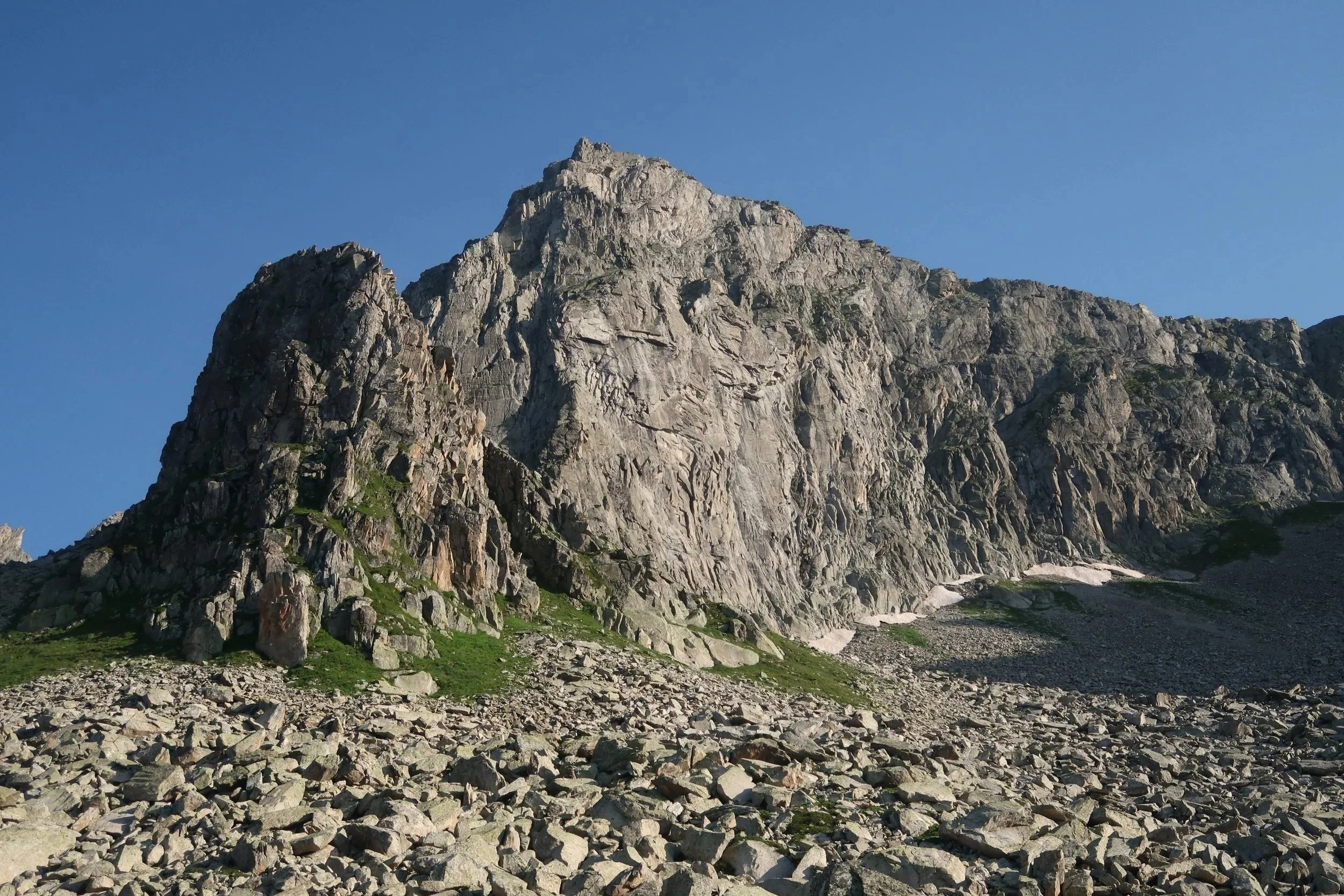 Berg mit steilen Felswänden und einer felsigen, grasbedeckten Talregion, unter klarem blauen Himmel