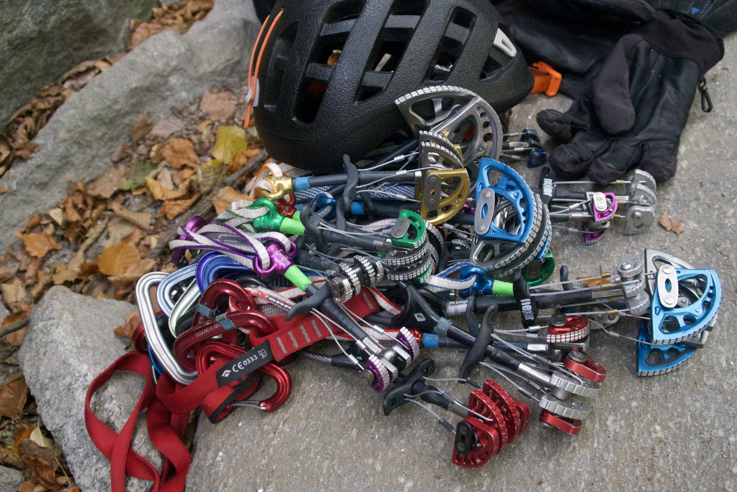 Ein Haufen Kletterausrüstung, einschließlich Karabiner, Steigeisen, Kletterhelm, Gurtzeug und Handschuhe, liegt auf dem Boden im Freien.