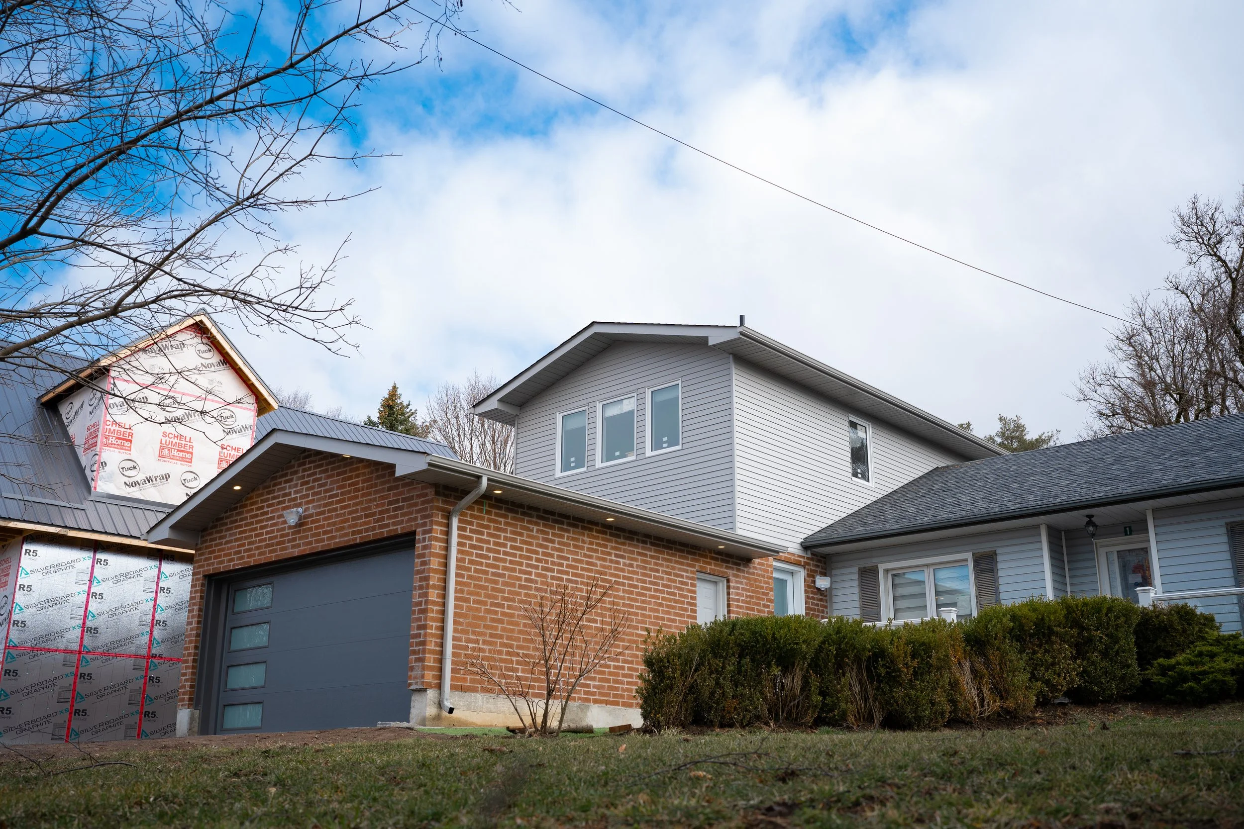 Exterior of a house under construction, with brick and siding, a garage door, and bare trees in the yard.