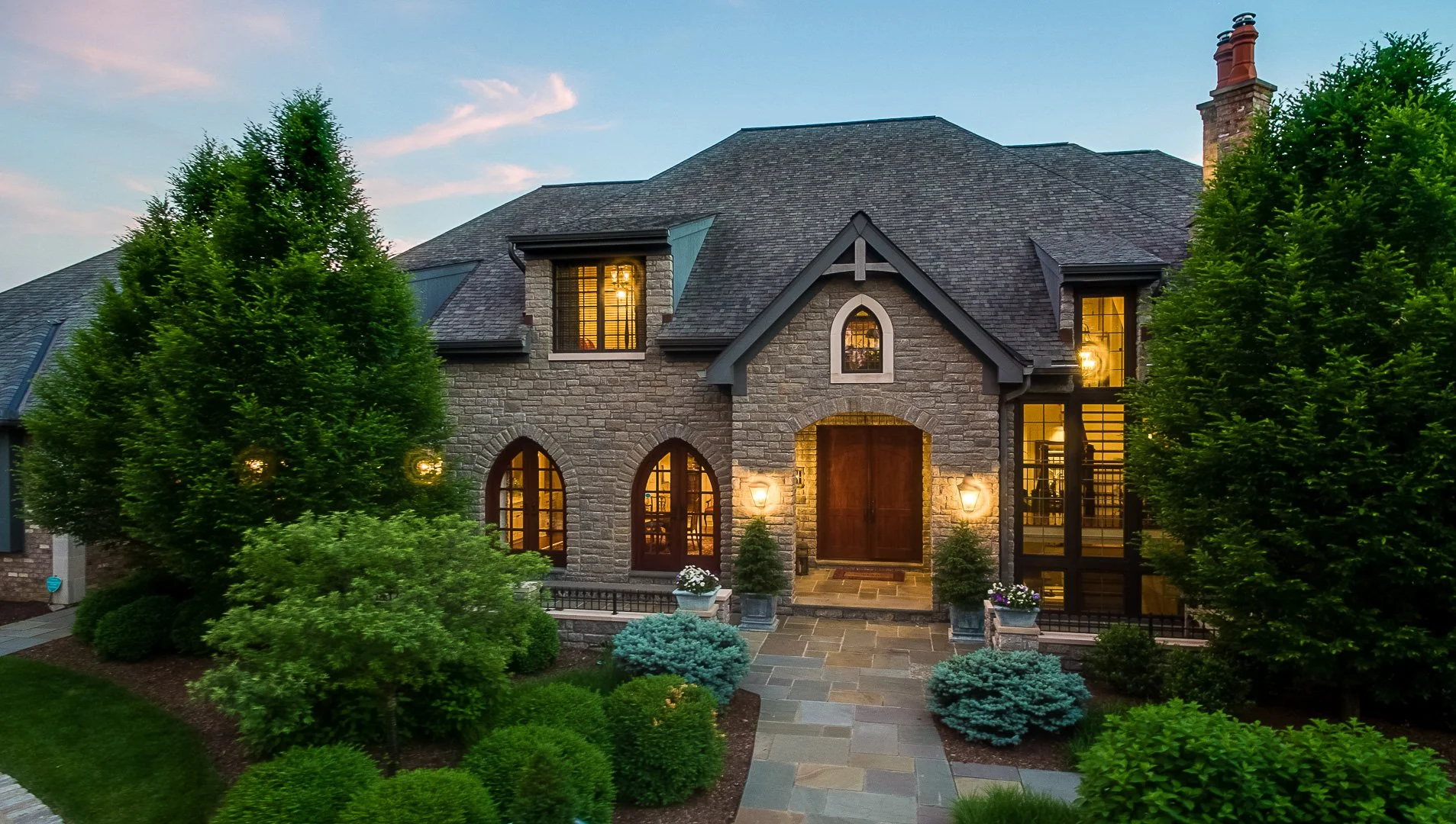 Stunning twilight exterior of a luxury stone home with lush landscaping, showcasing professional real estate photography services perfect for marketing high-end property listings and lifestyle-focused visuals.