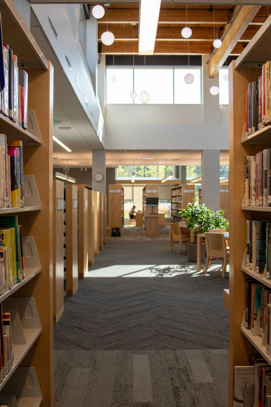 A brightly lit library, rows of books in light grained wooden bookshelves