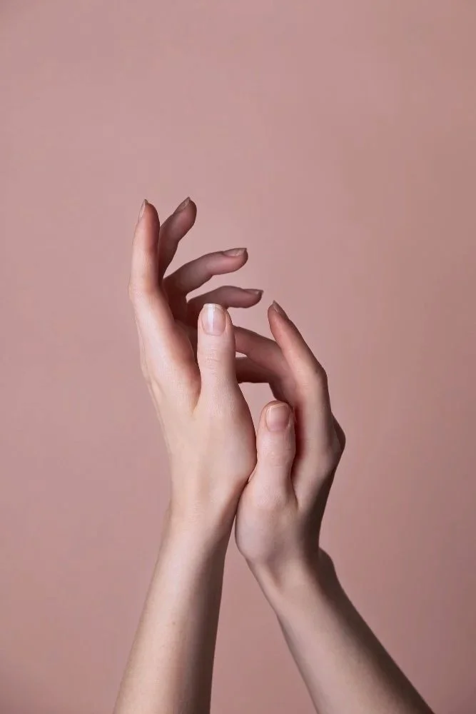 Close-up of two hands with interlocked fingers against a plain, soft pink background.