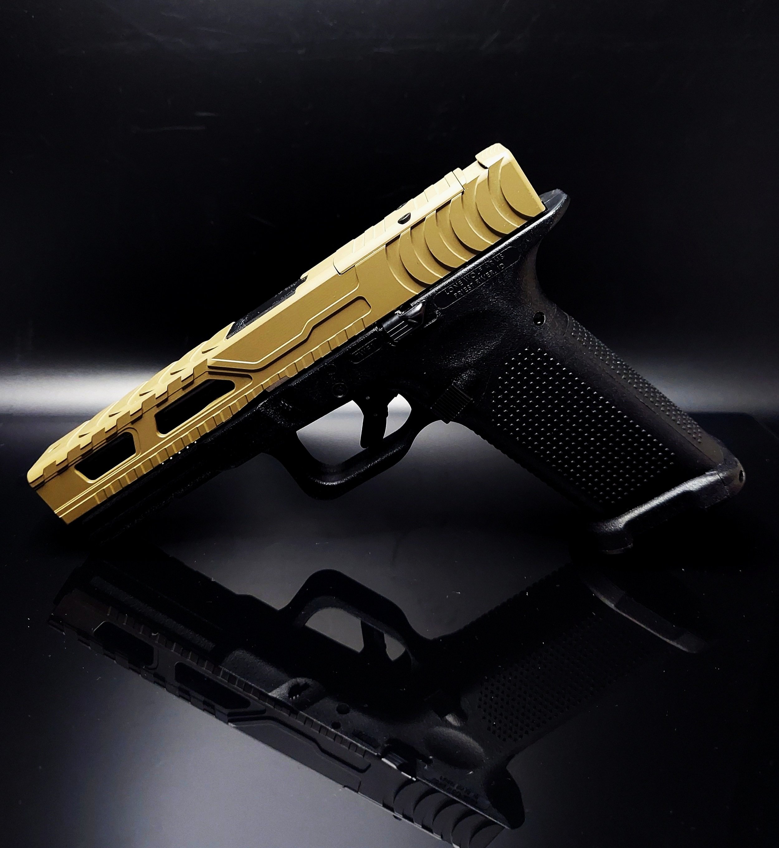 A black and tan handgun with a textured grip, resting on a reflective black surface.