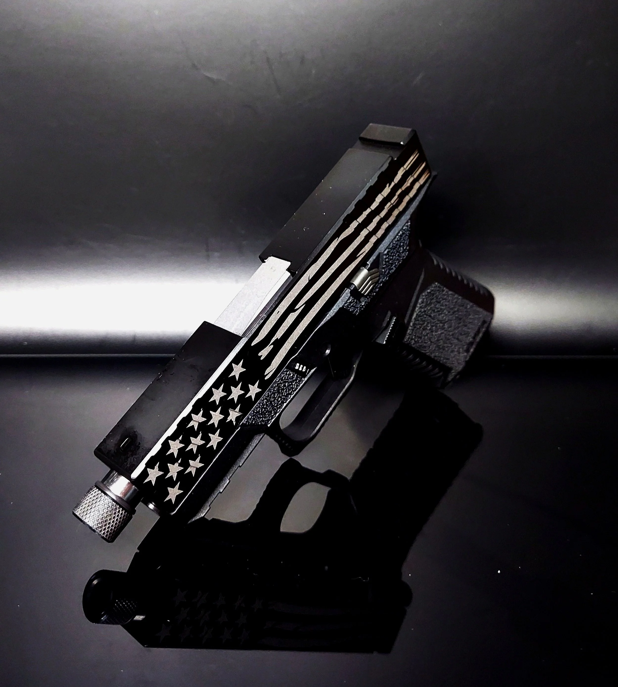 A black semi-automatic handgun with a star and stripe pattern on the slide, resting on a reflective black surface.