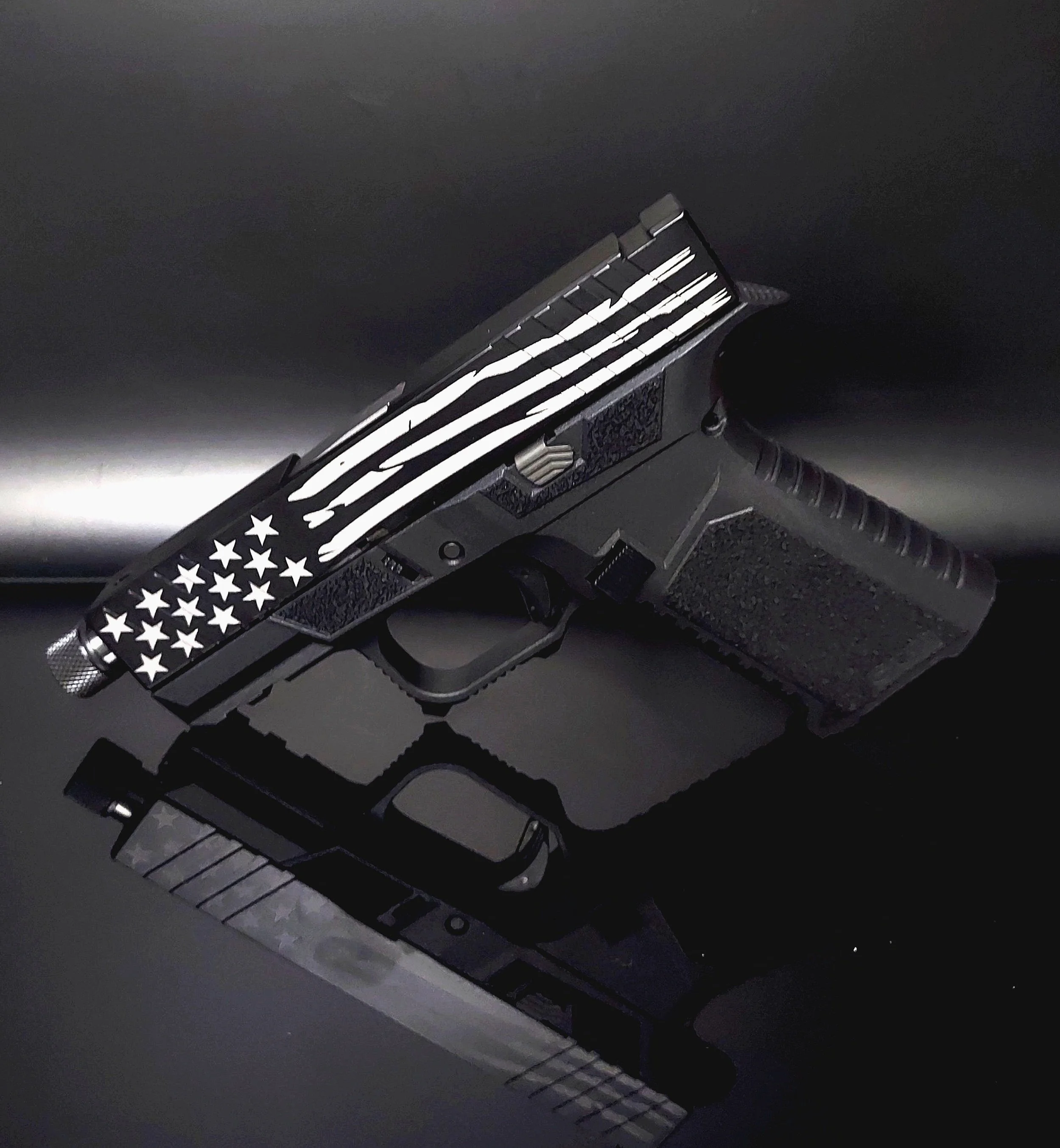 A black handgun with an American flag design on the slide, resting on a reflective black surface.